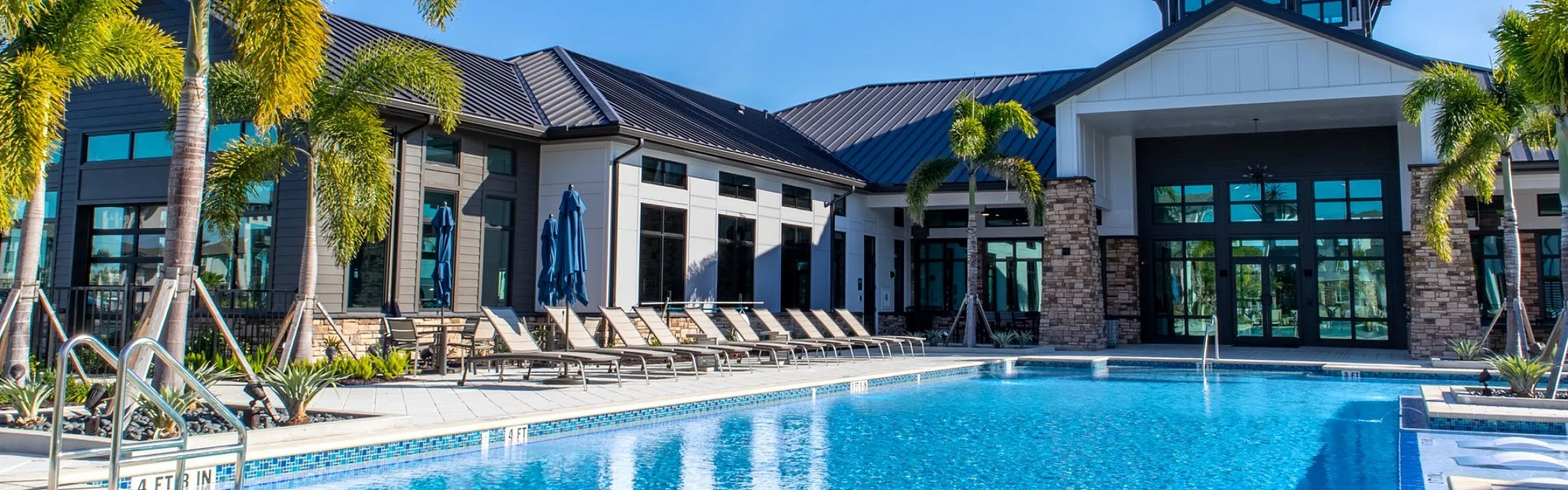 Luxurious apartment building exterior with a sparkling pool, surrounded by lush palm trees and modern architecture.