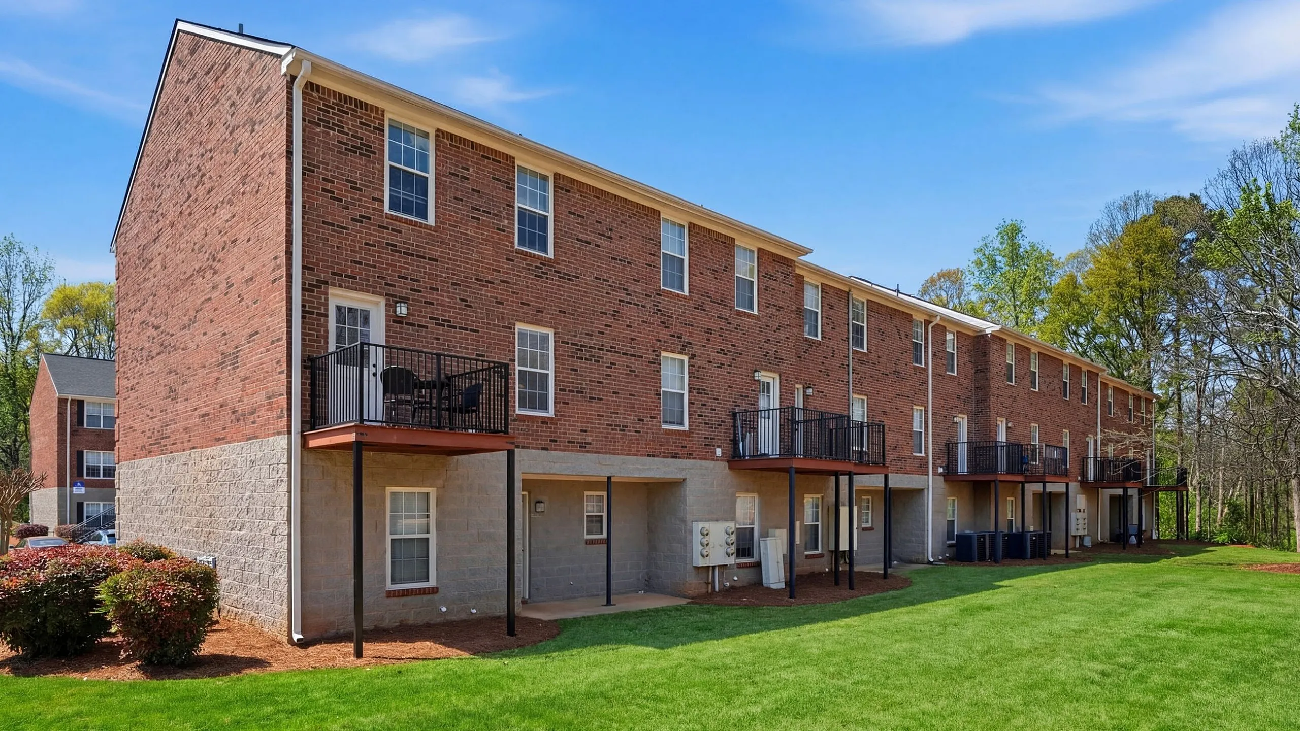 Charming brick apartment complex with spacious balconies overlooking lush green landscape, perfect for enjoying the outdoors.