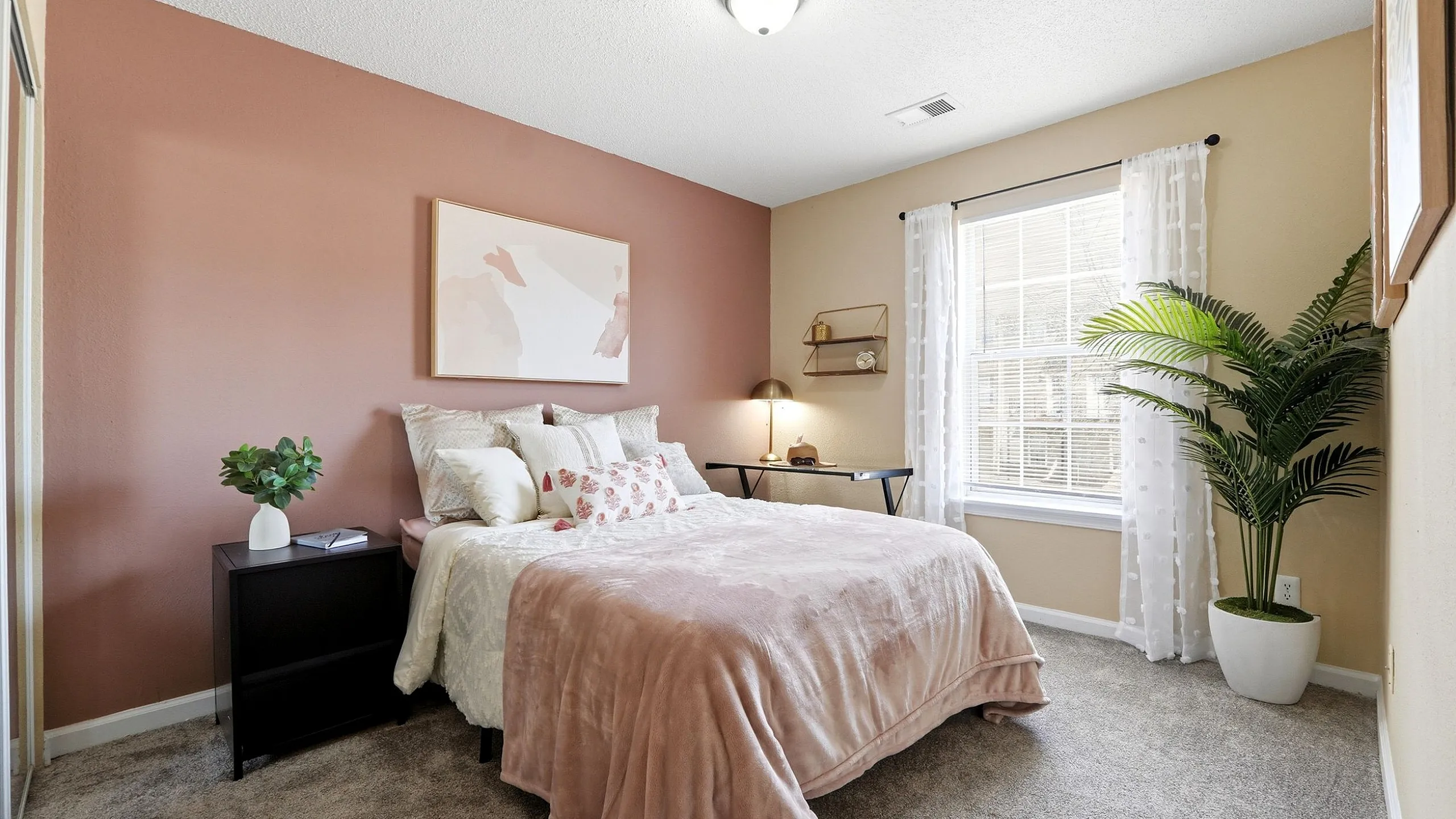 Inviting bedroom with elegant decor, featuring a cozy bed, stylish pink accent wall, and abundant natural light.