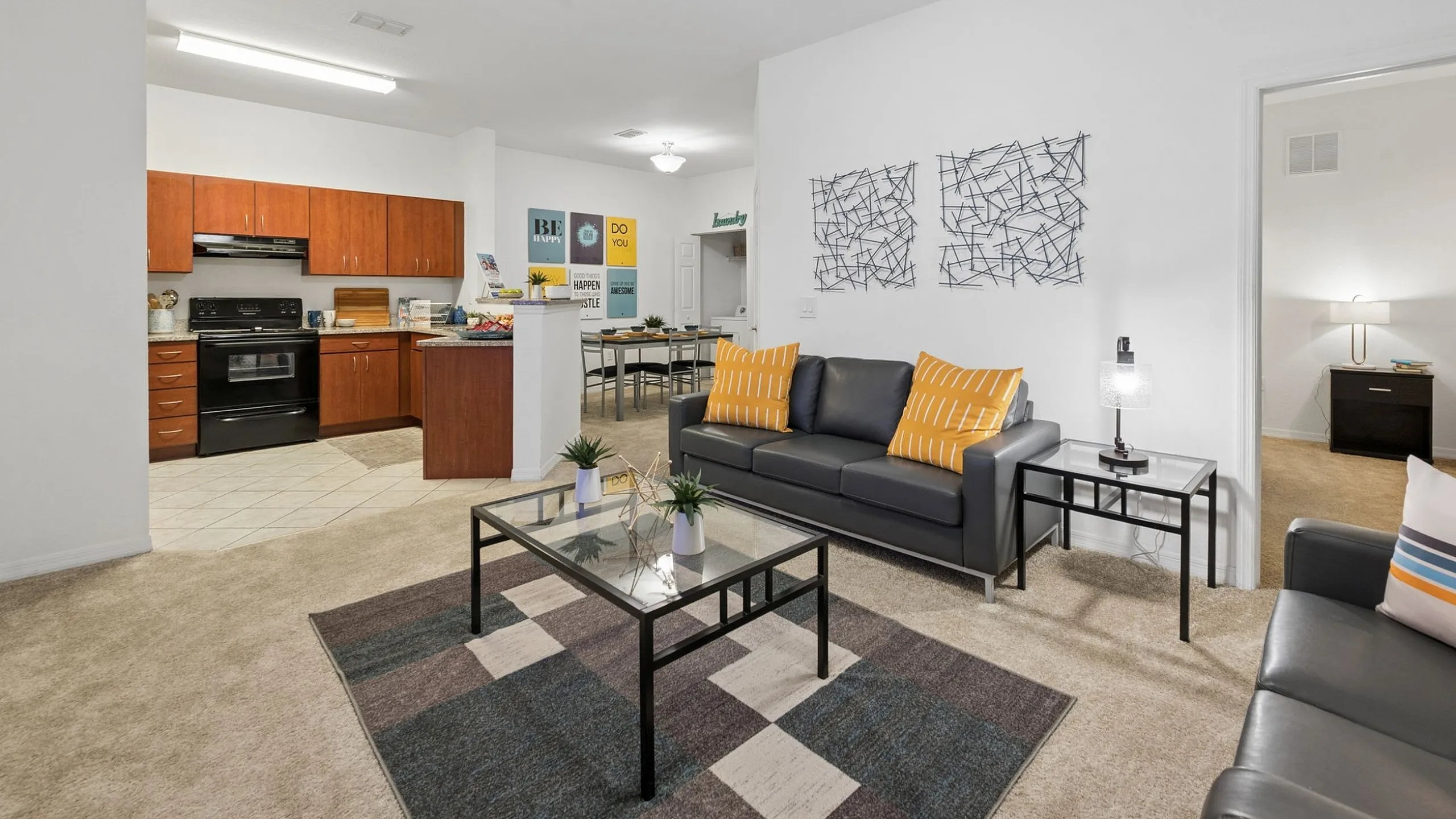 Inviting apartment interior showcasing an open-concept living room with modern furnishings, vibrant artwork, and cozy decor connecting seamlessly to a spacious kitchen with sleek wooden cabinets and contemporary appliances.