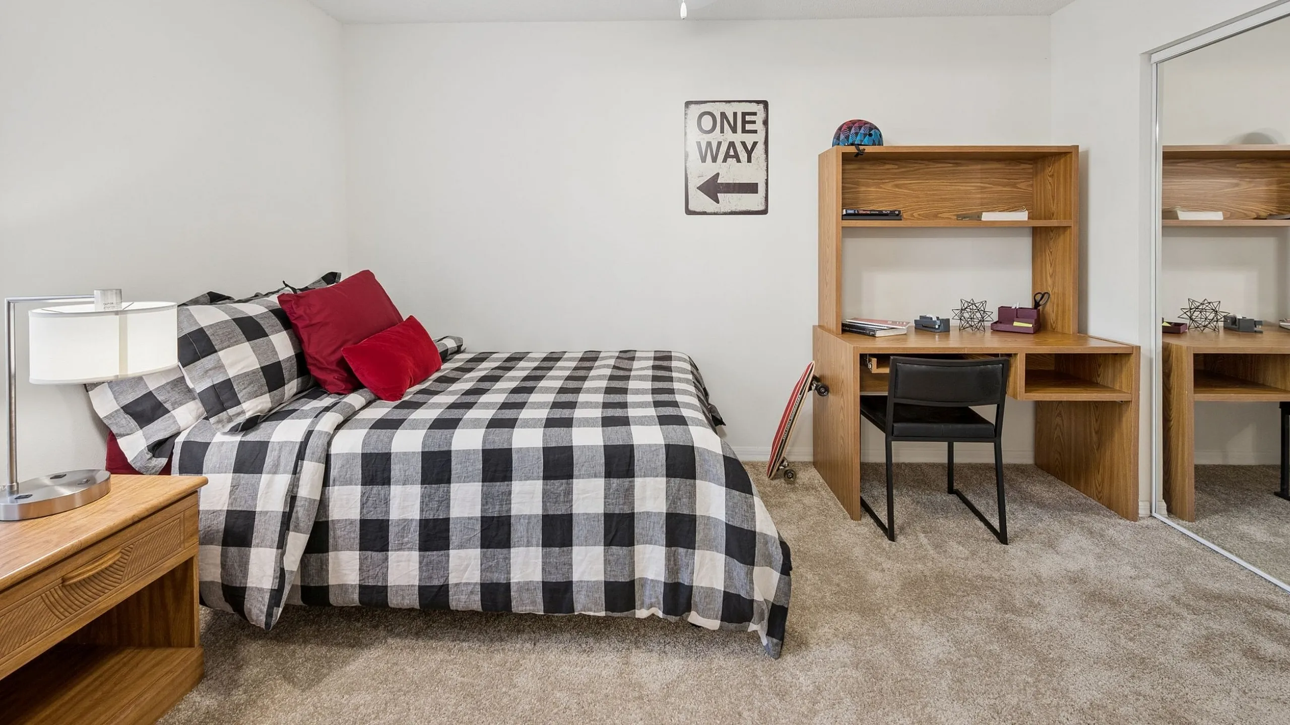 Inviting bedroom with cozy checkered bedspread, sleek wooden desk, and mirrored closet doors, creating a warm and functional living space.
