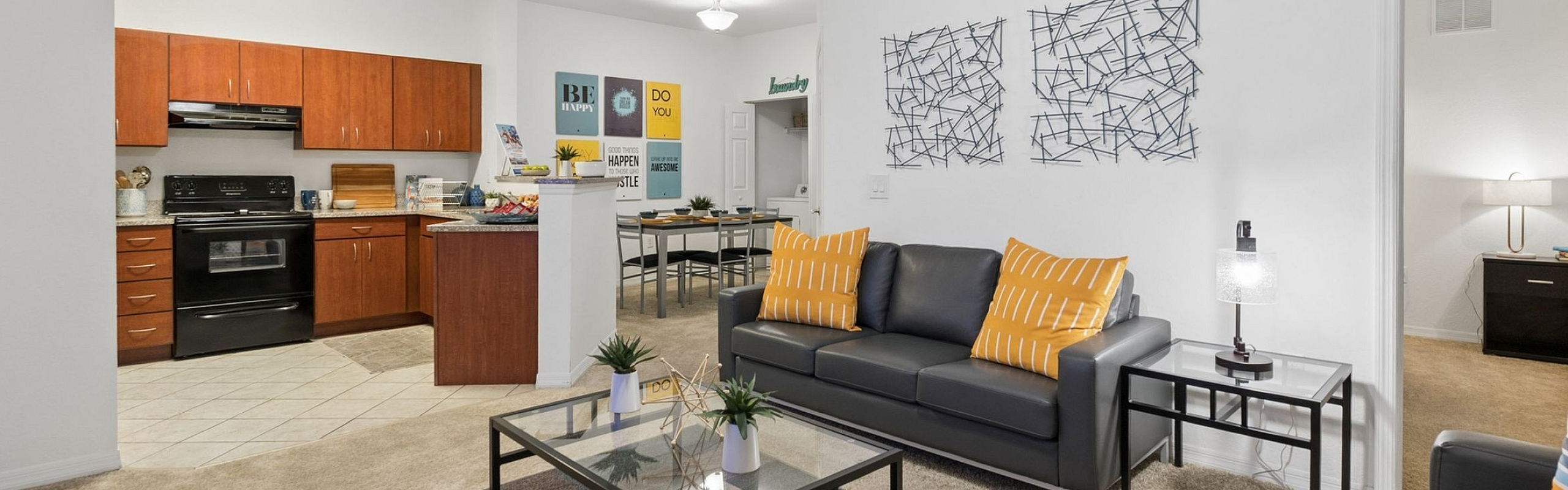 Modern apartment with sleek open-concept design featuring a cozy living area, stylish gray sofas, vibrant yellow accents, and a well-equipped kitchen with warm cabinetry.