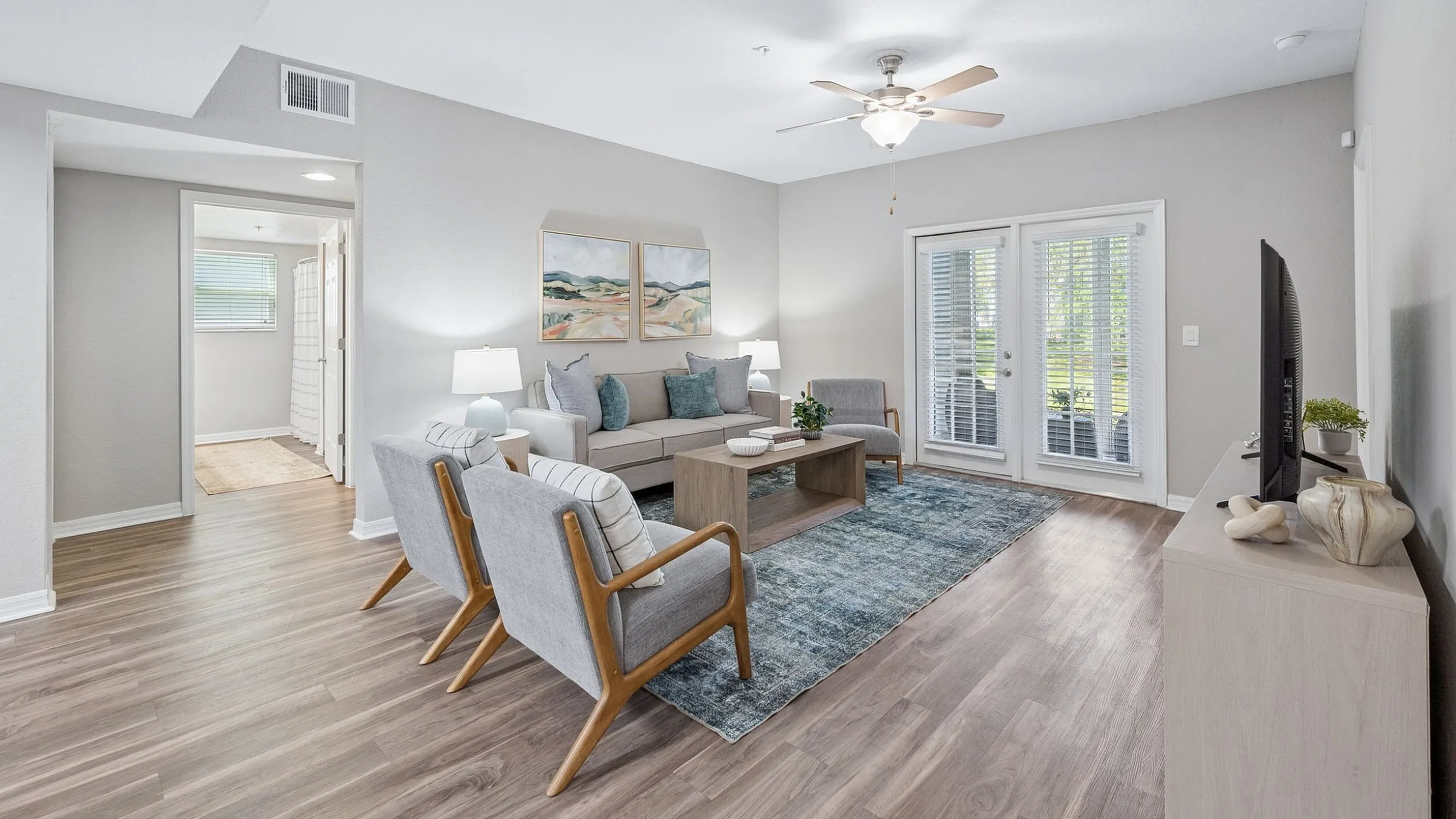 Bright and inviting living room with stylish wooden flooring, modern furniture, and abundant natural light through large glass doors.