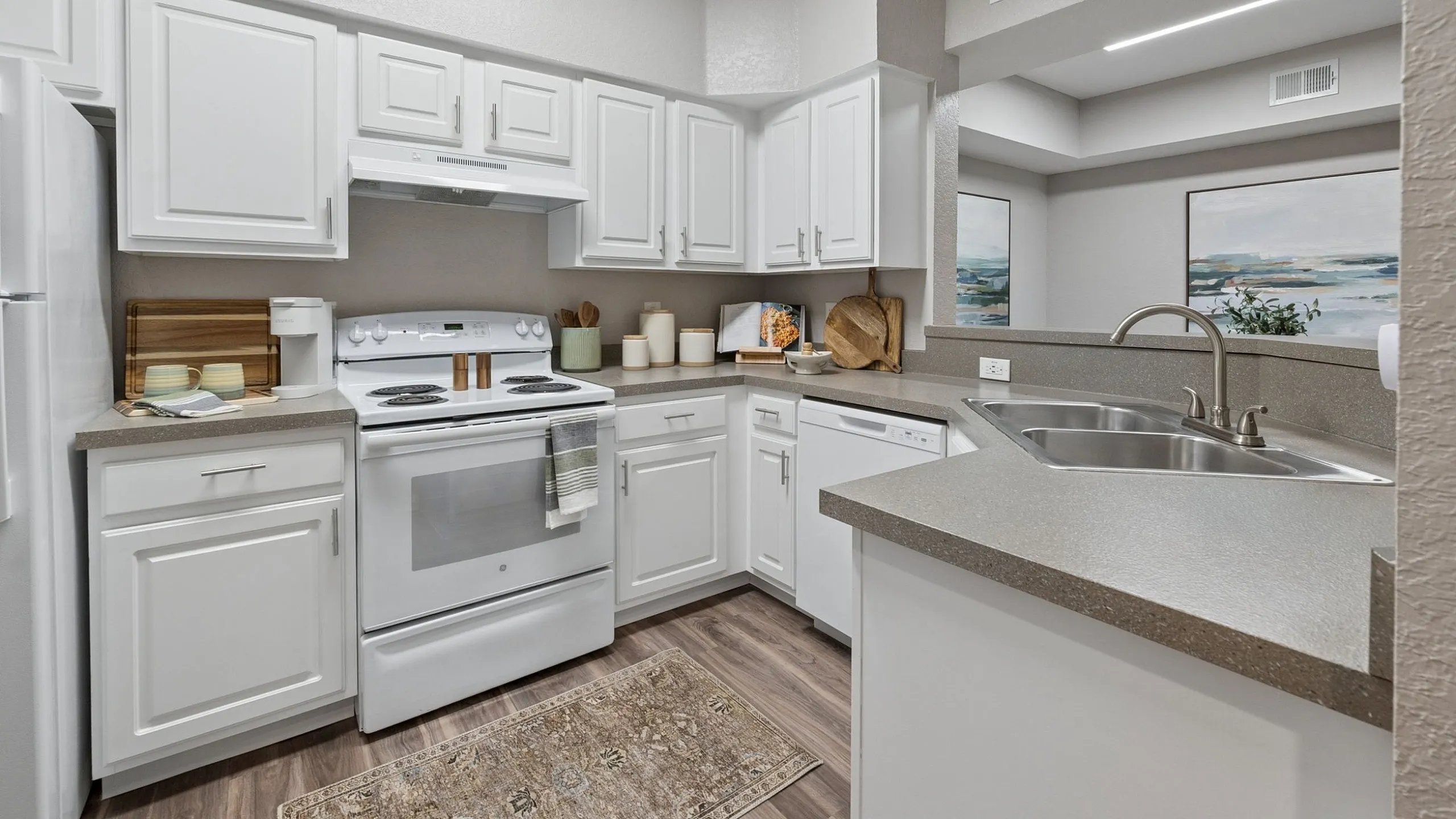 Modern kitchen with sleek white cabinetry, spacious countertops, and stainless steel sink, featuring elegant wood flooring and stylish decor.