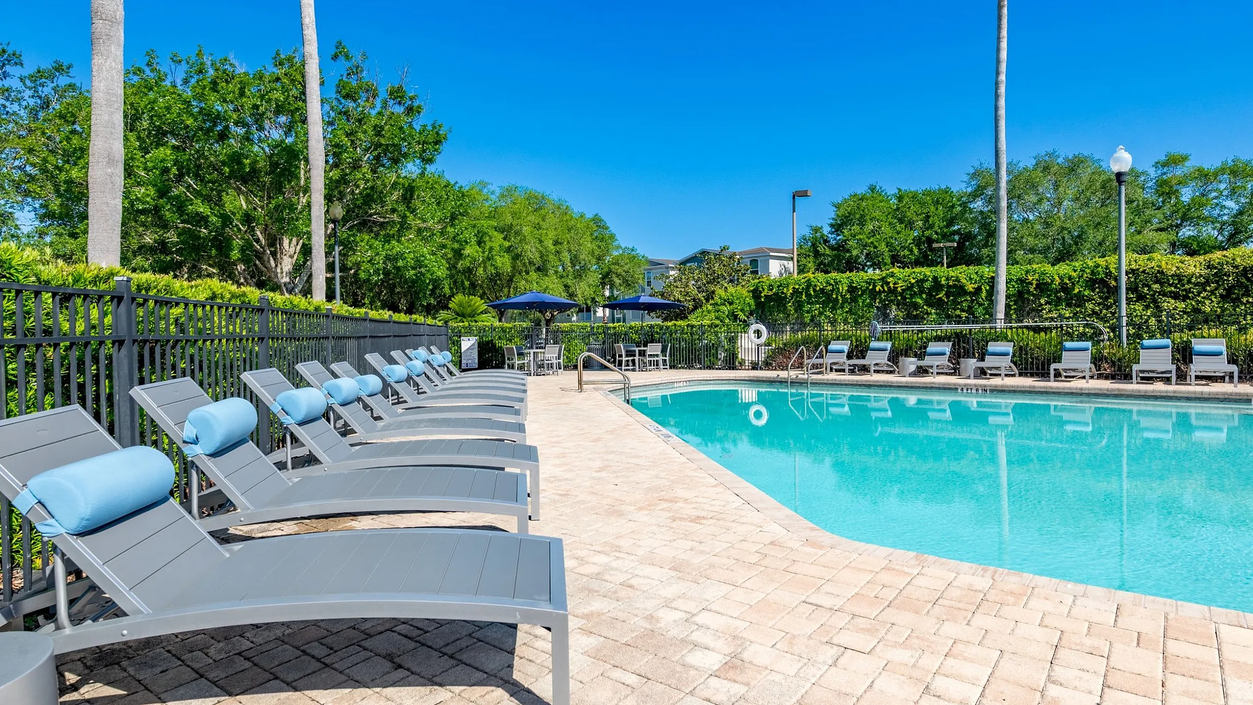 Luxurious outdoor pool area with stylish loungers and lush greenery under a bright blue sky, perfect for relaxation and leisure.