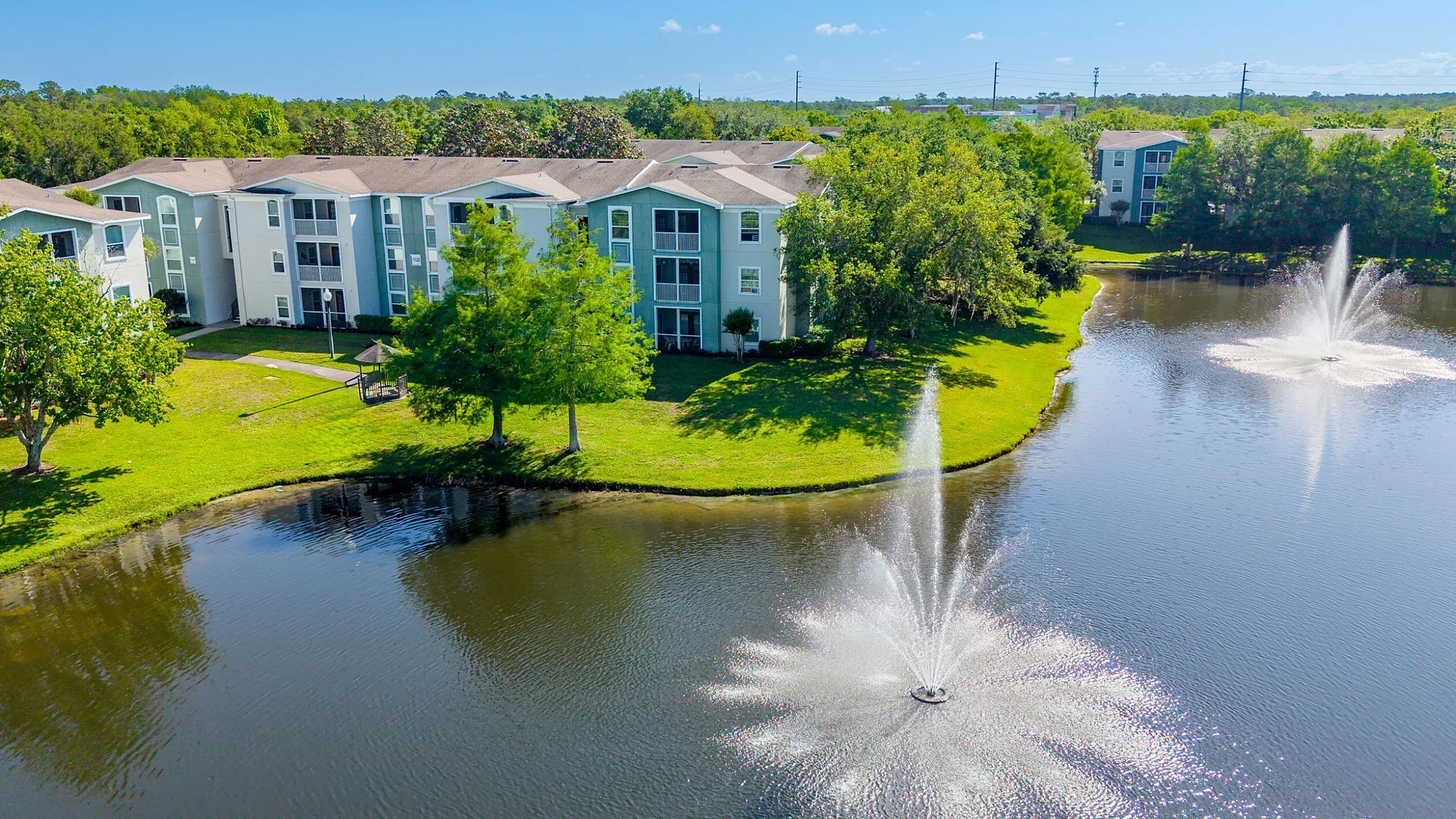 Charming lakeside apartments with lush green surroundings and serene water fountains.
