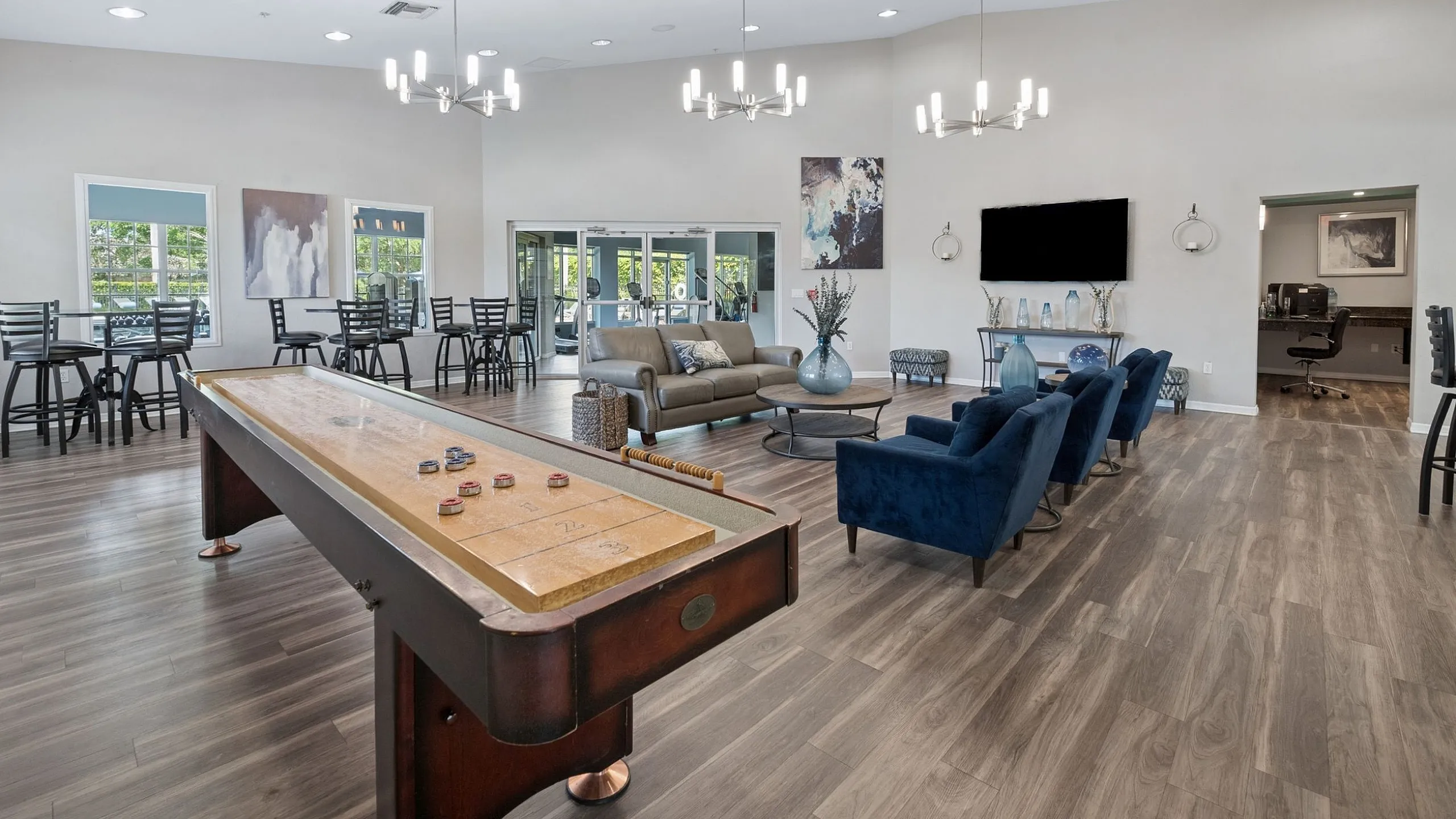 Spacious, modern lounge area with elegant wood flooring, inviting seating, and a stylish shuffleboard table perfect for entertainment.