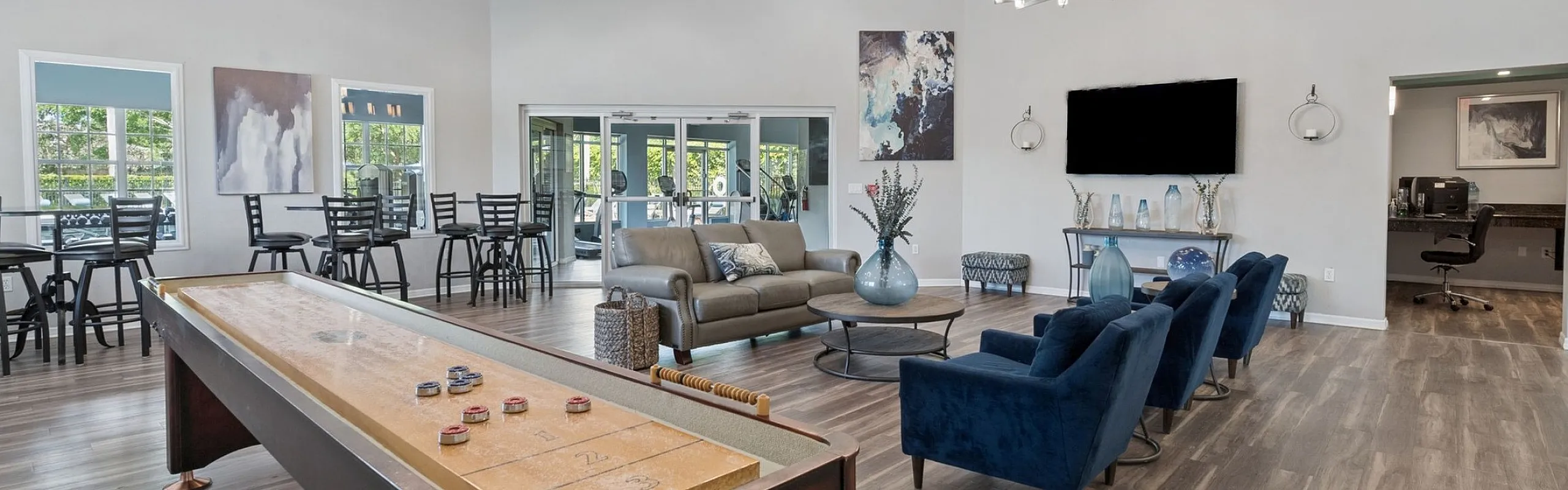 Luxurious common room featuring a shuffleboard table, stylish seating with blue velvet chairs, and bright, modern decor.