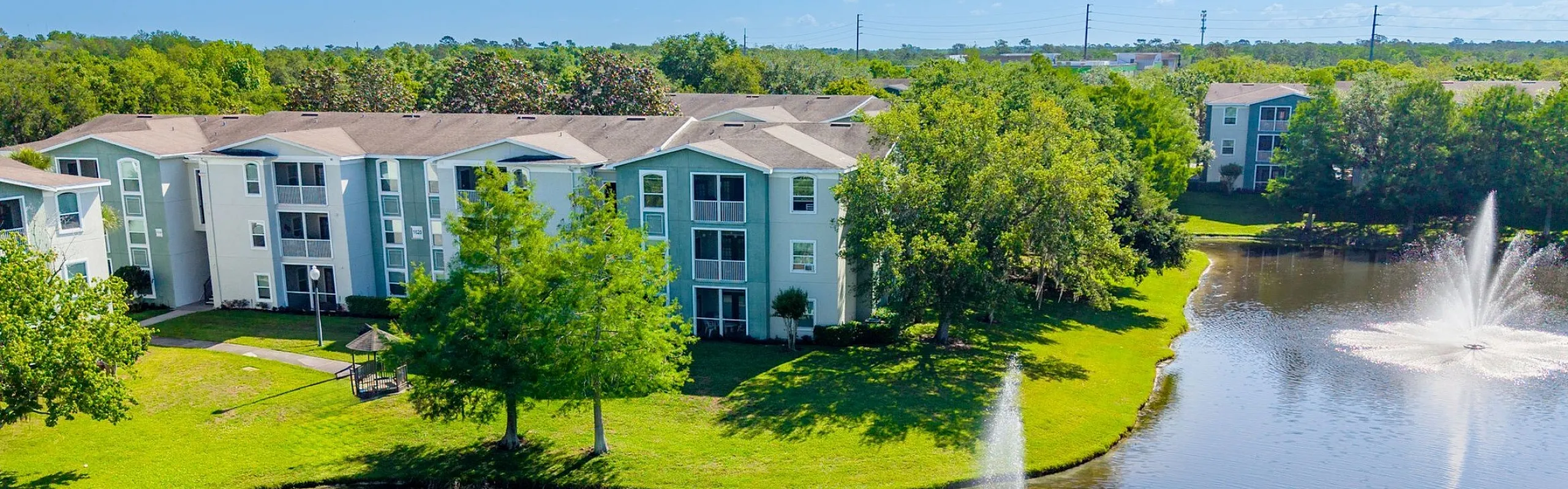 Serene apartment complex with scenic water fountains and lush greenery, offering tranquil lakeside living.