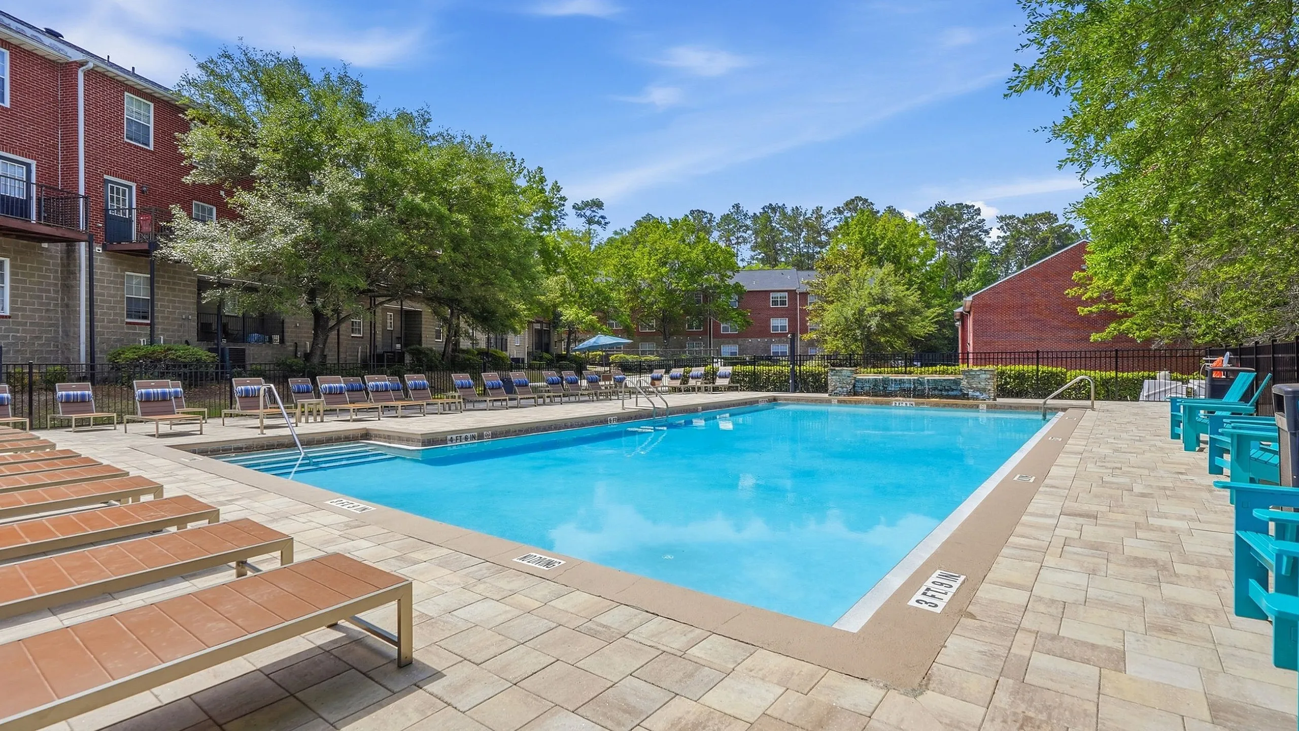 Inviting community pool surrounded by chic lounge chairs and lush greenery, perfect for relaxation and enjoyment.