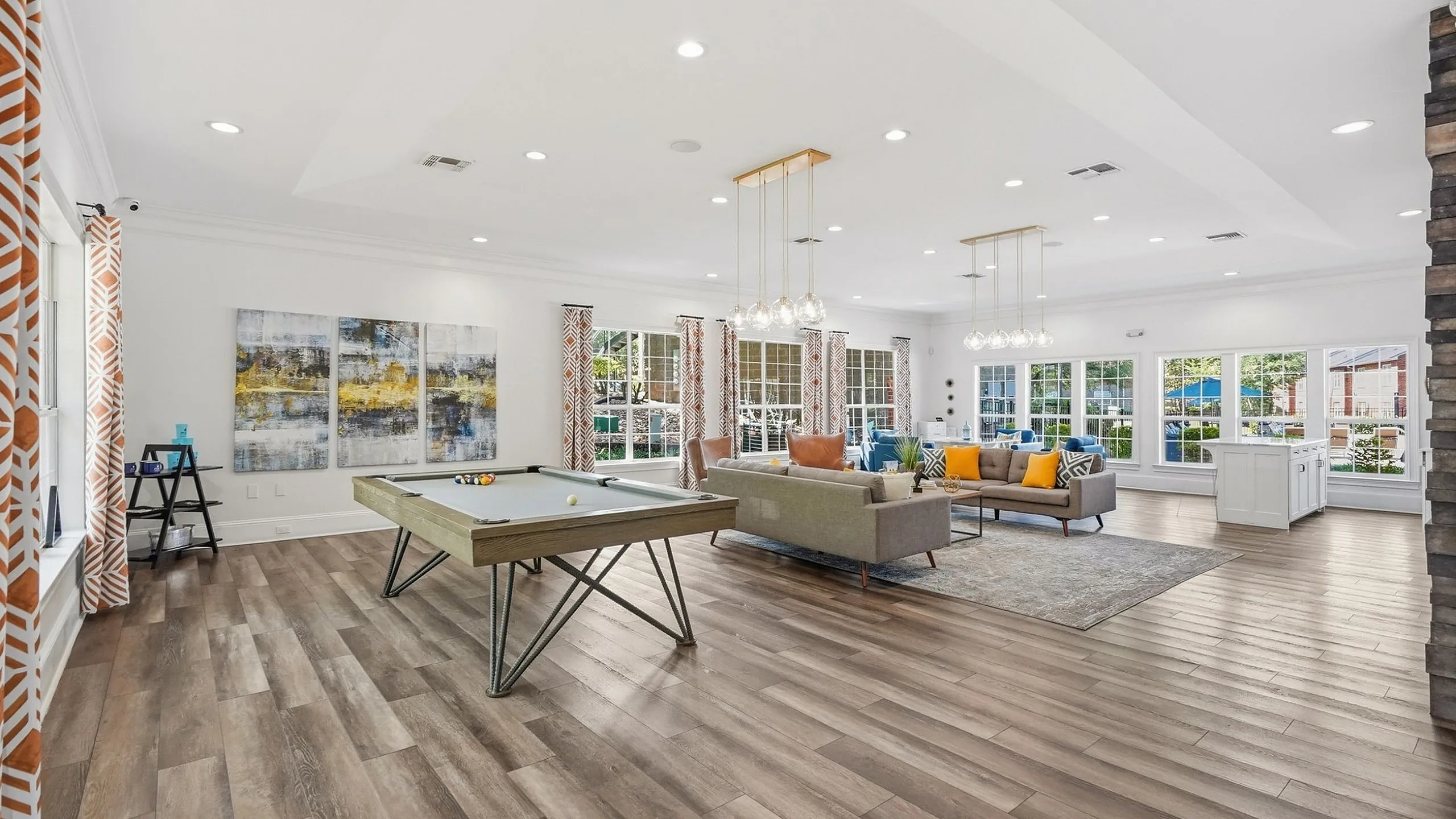 Spacious, modern living area featuring sleek wood flooring, stylish pool table, and vibrant decor with ample natural light.