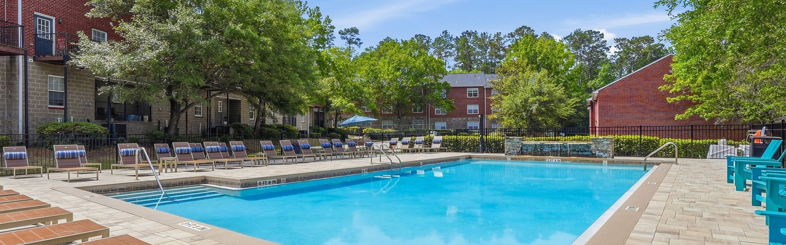 Inviting outdoor pool area with sun loungers, surrounded by lush greenery and stylish brick apartments.