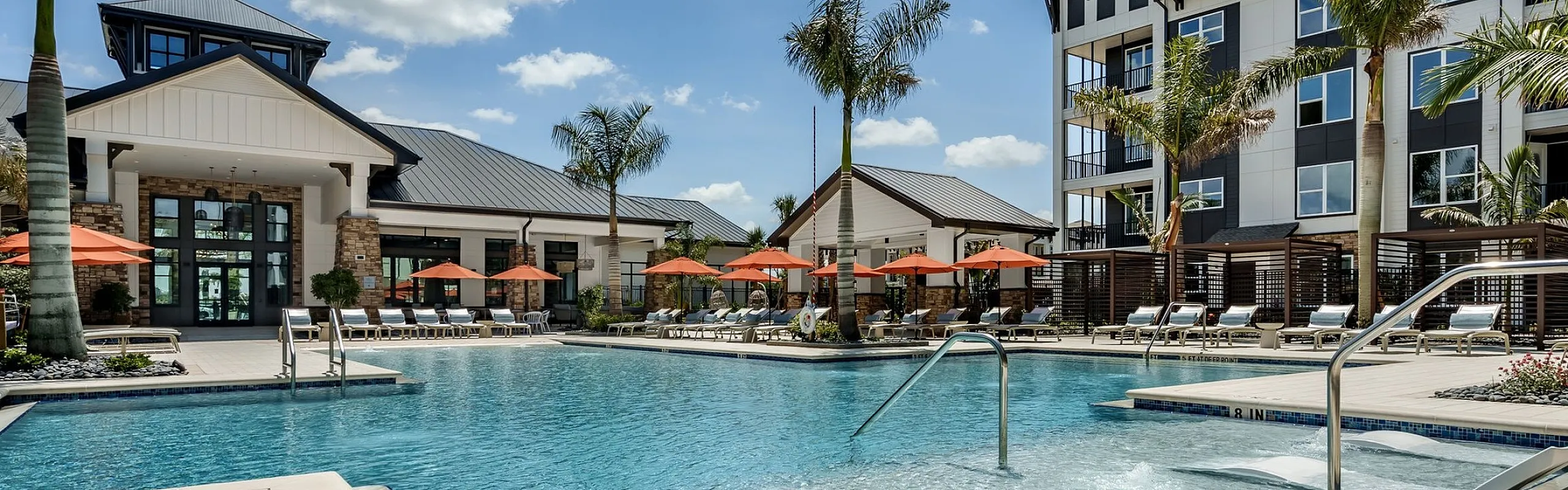 Luxurious apartment complex featuring a dazzling swimming pool with sun loungers, surrounded by palm trees and chic modern architecture.