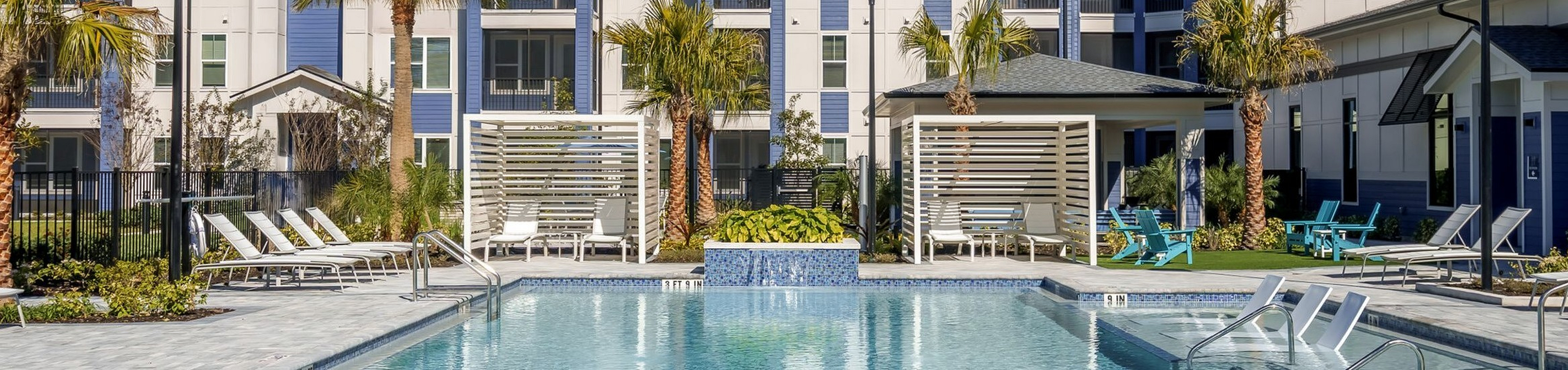 Luxurious apartment complex with a resort-style swimming pool, modern architecture, and inviting palm trees.