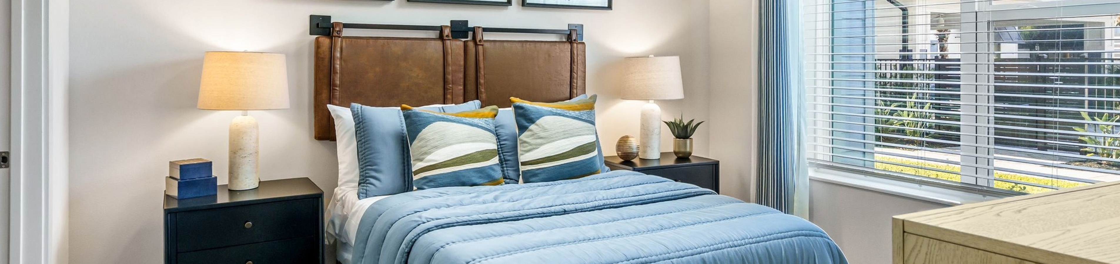Bright and inviting bedroom with elegant decor, featuring a cozy bed with blue linens, artistic wall art, and a sunlit window.