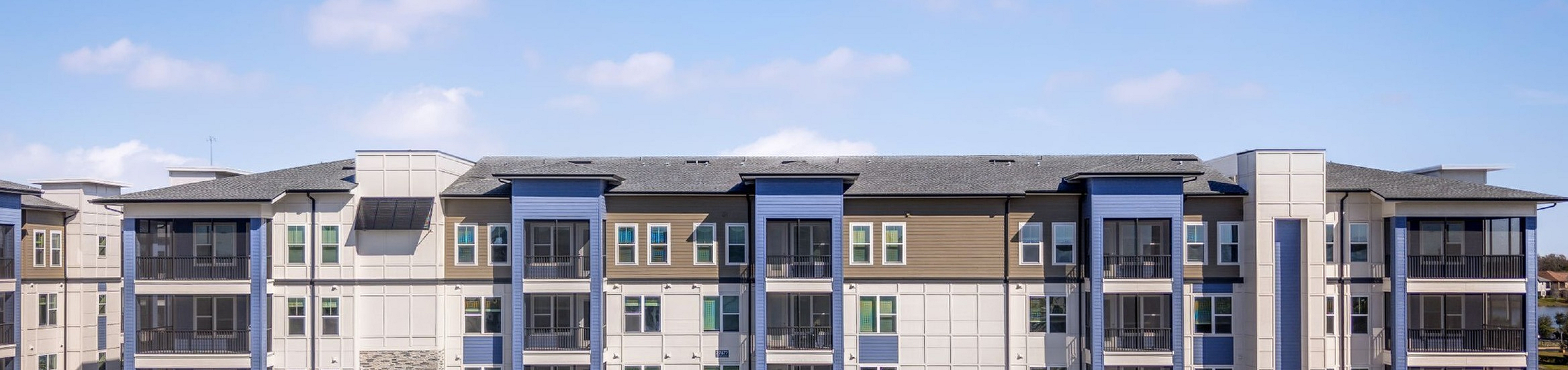 Modern apartment complex with sleek architectural design, large windows, and well-maintained landscaping under a bright blue sky.