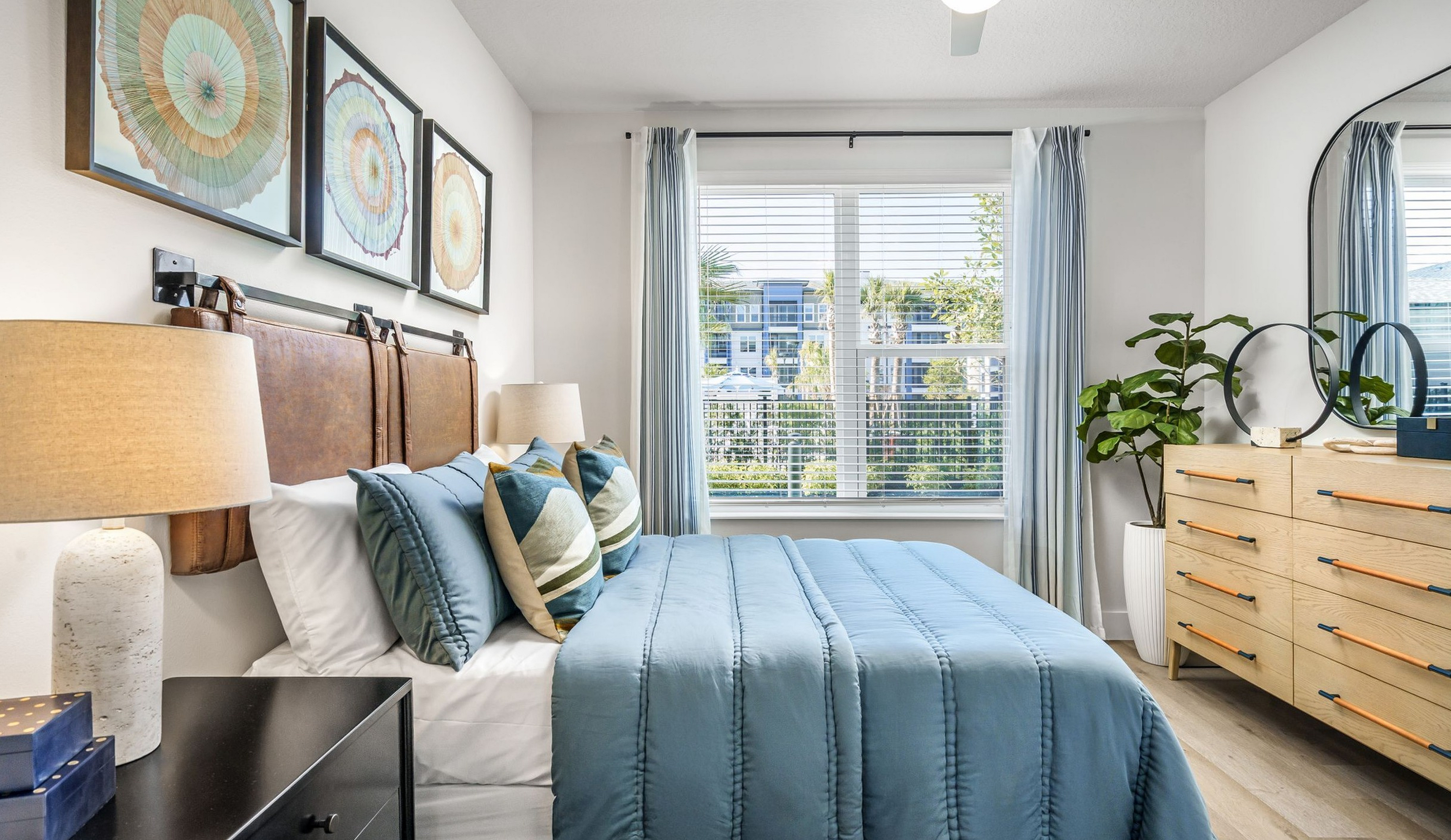 Bright and inviting apartment bedroom with modern decor, featuring a large window, elegant artwork, and stylish furnishings.
