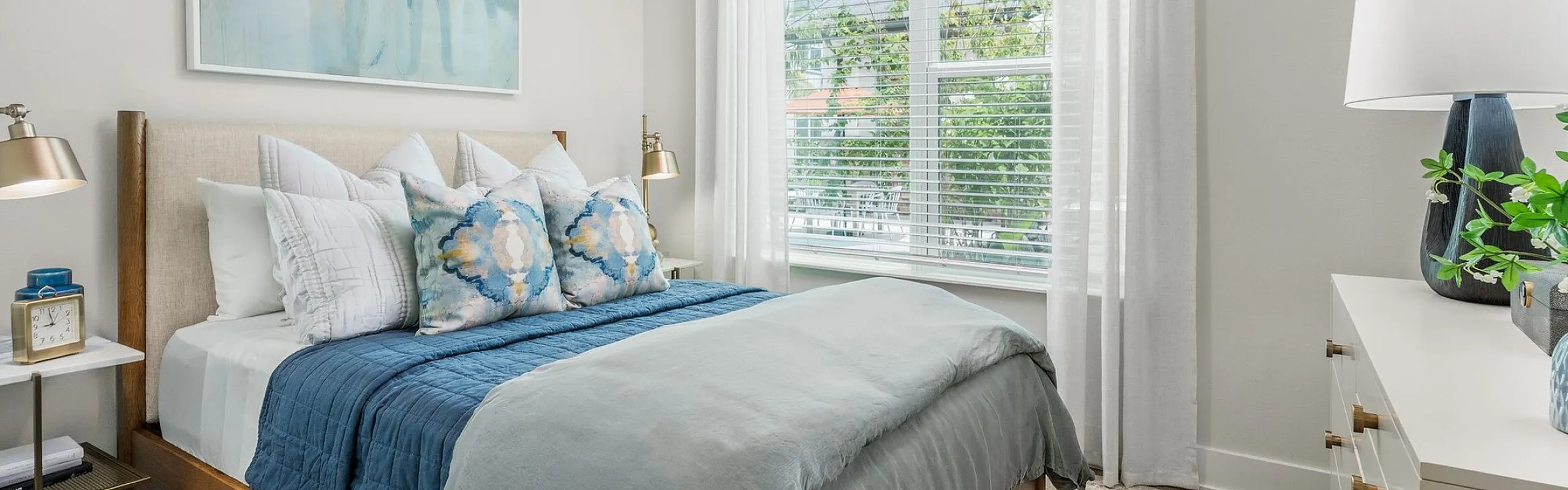 Bright and inviting bedroom with modern decor, featuring a cozy bed, contemporary art, and large windows that fill the space with natural light.
