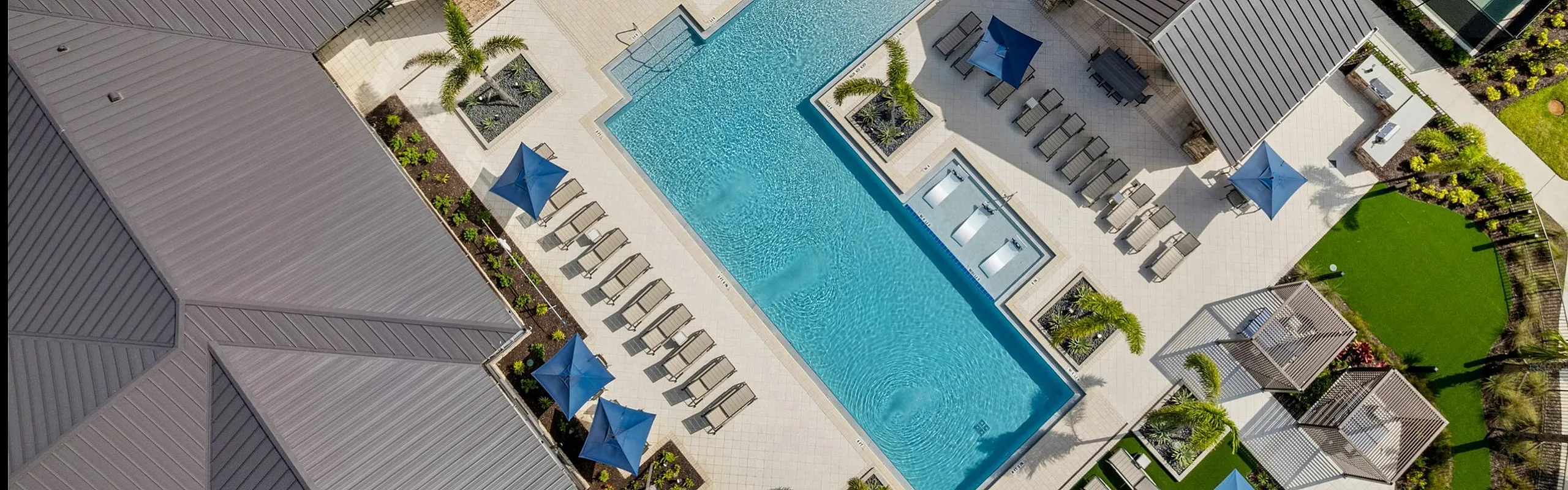 Aerial view of a luxurious apartment complex featuring a stunning swimming pool with lounge chairs, lush landscaping, and a tennis court for residents to enjoy.