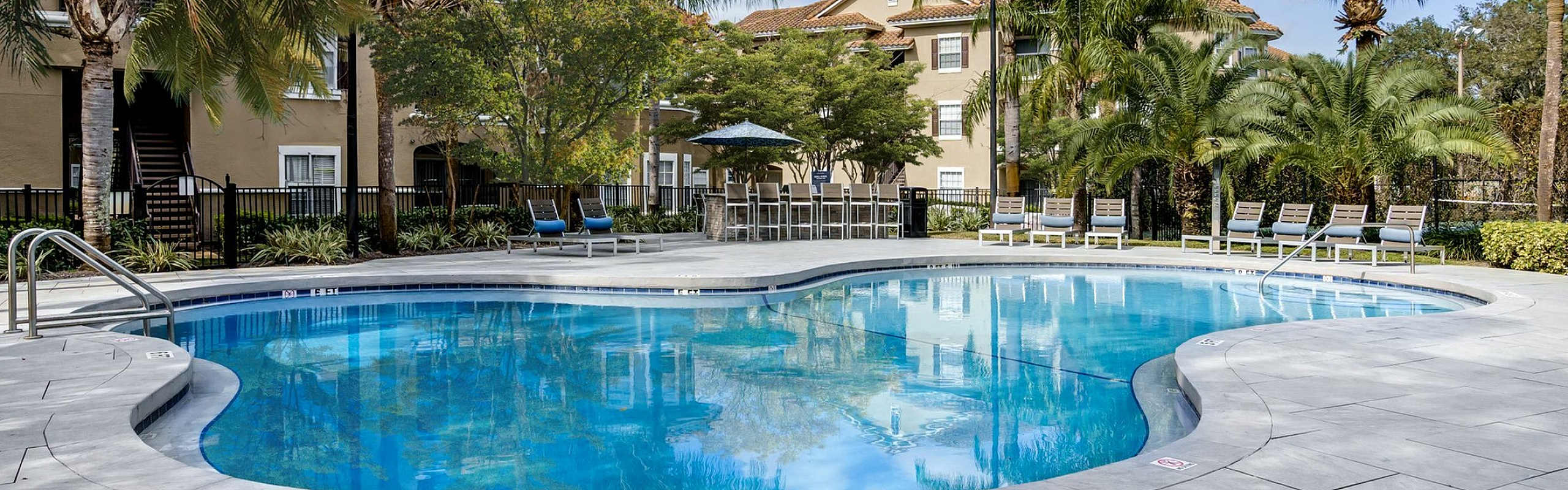 Inviting apartment complex featuring a sparkling pool surrounded by lush palm trees and comfortable lounge seating.