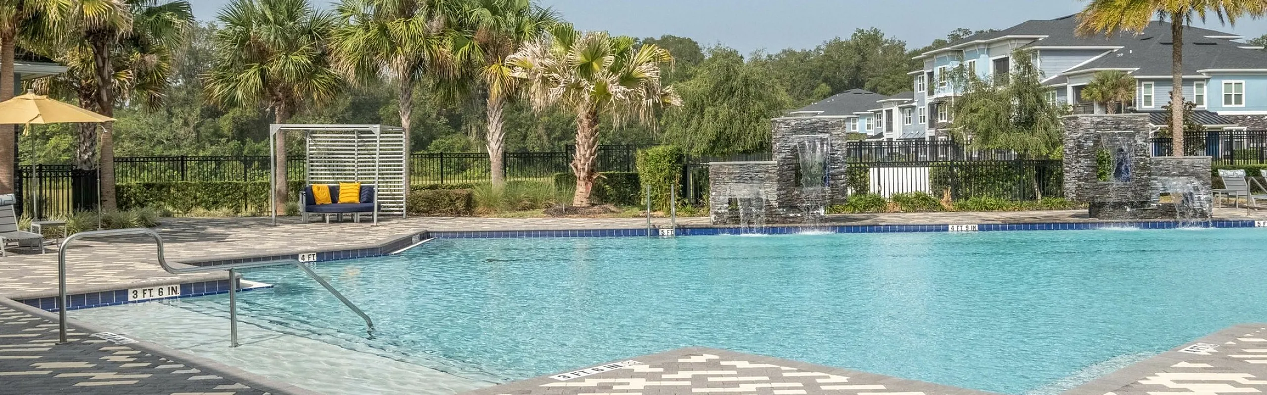 Luxurious swimming pool surrounded by lush palm trees and modern apartments, ideal for relaxation and leisure.