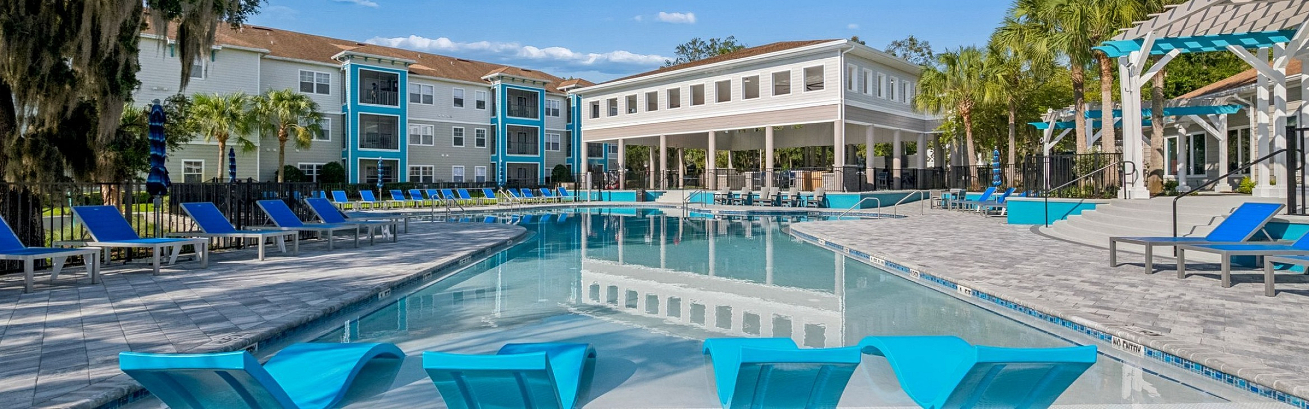 Luxurious apartment complex with a stunning outdoor pool, stylish lounge chairs, and beautifully landscaped surroundings.