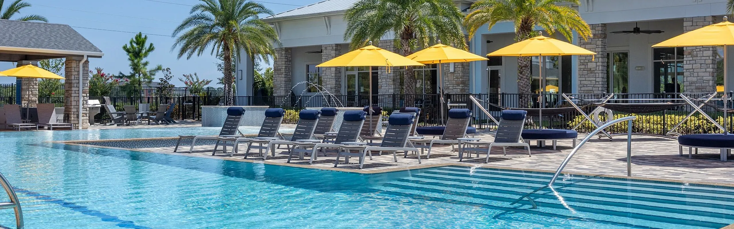 Luxurious resort-style pool area with vibrant yellow umbrellas, palm trees, and sleek lounge chairs, perfect for relaxation.