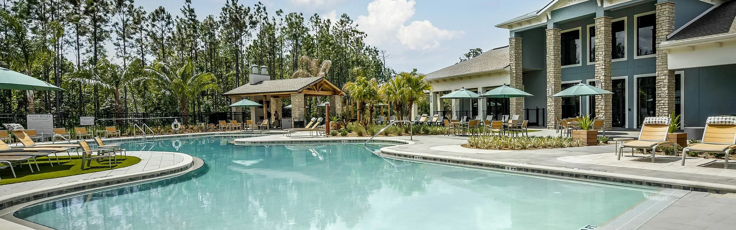 Luxurious apartment complex featuring a sparkling outdoor pool, surrounded by comfortable sun loungers and shaded seating areas, set amidst lush greenery.