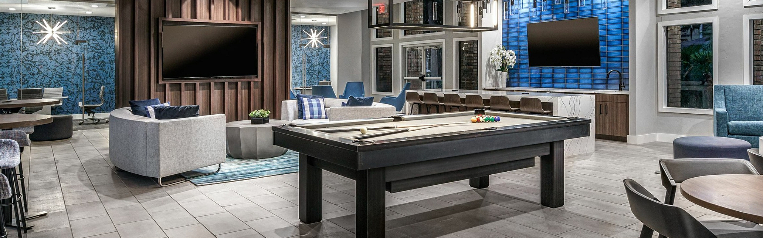 Sleek and modern recreation room with stylish ceiling beams, a billiard table, plush seating, and dual flat-screen TVs, perfect for entertaining.