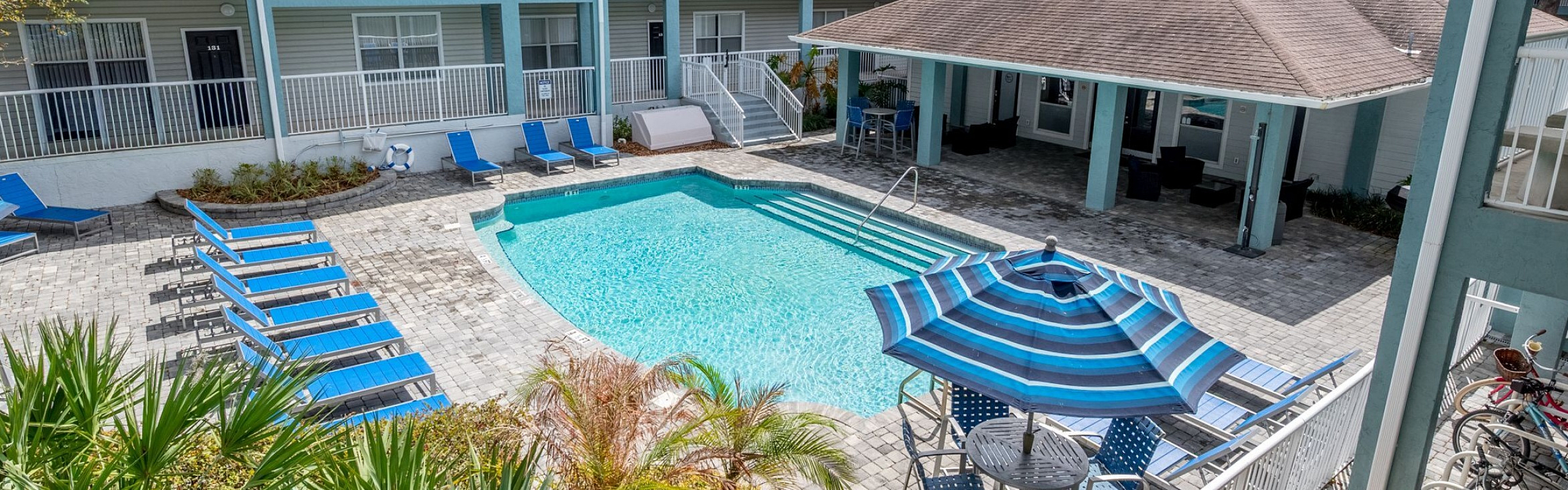 Inviting apartment complex featuring a sparkling swimming pool surrounded by modern blue sun loungers and shaded seating areas.