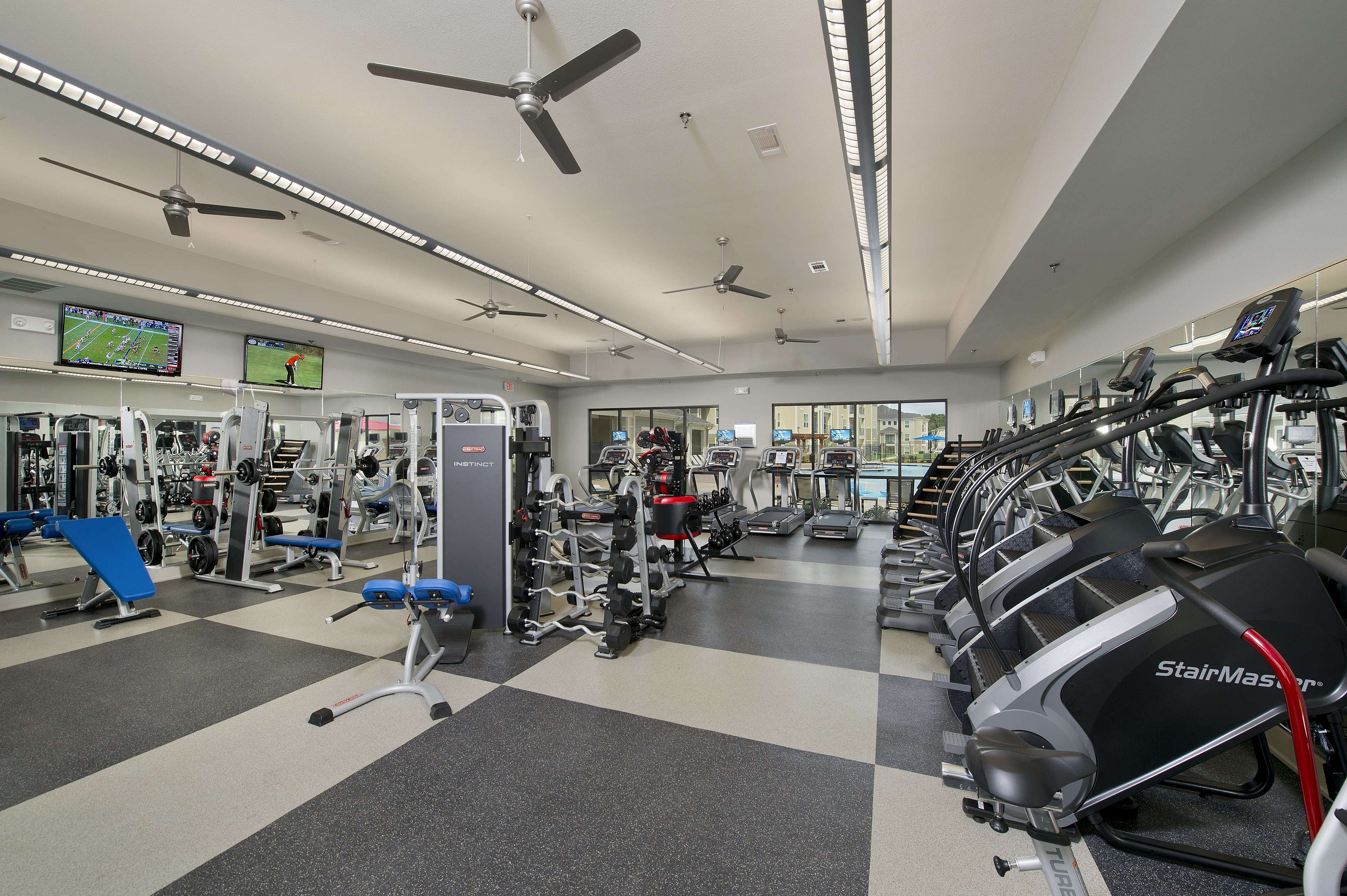 Modern fitness center equipped with a variety of cardio machines, weight training equipment, and high ceilings for a spacious workout experience.