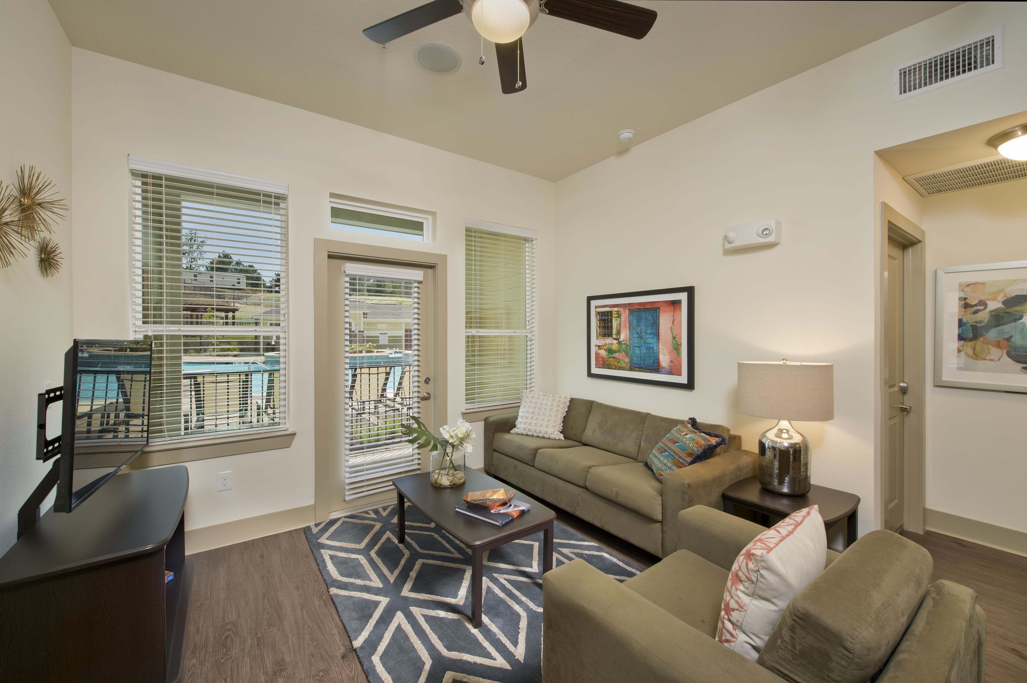 Chic living room featuring cozy beige sofas, elegant coffee table with a vase, vibrant wall art, and natural light streaming through large windows showcasing the pool view.