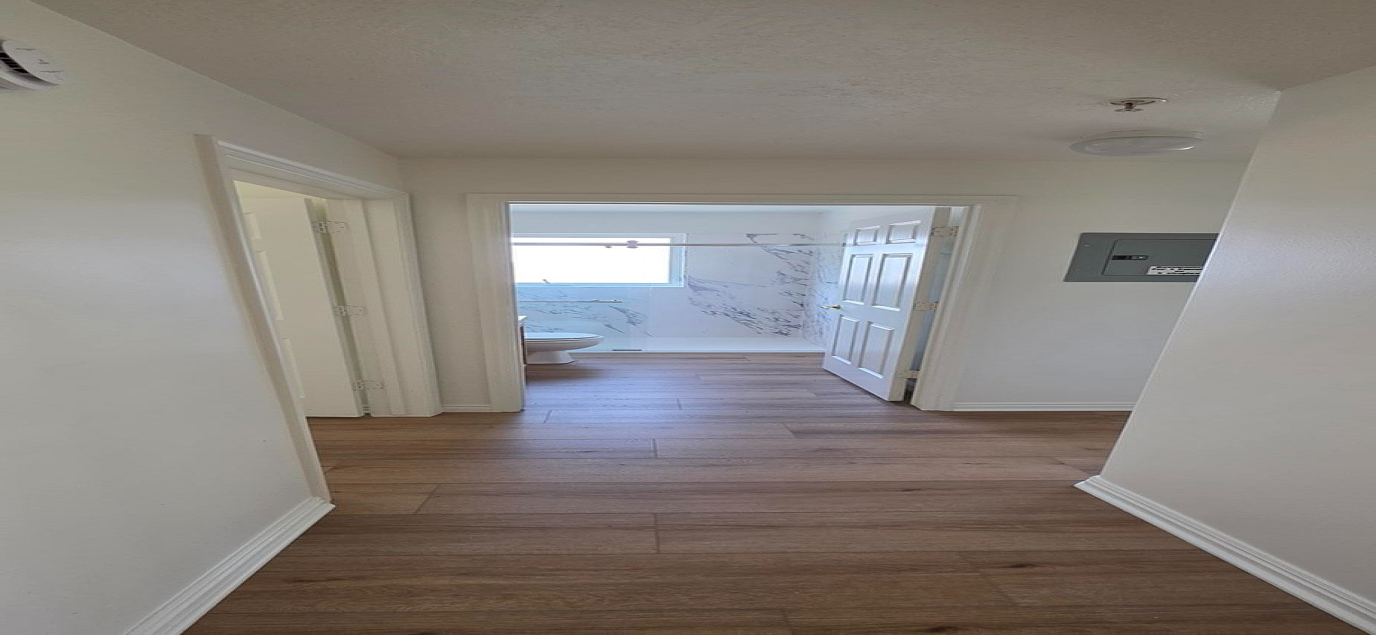 Inviting hallway with elegant wood flooring leading to a bright bathroom with modern marble accents.