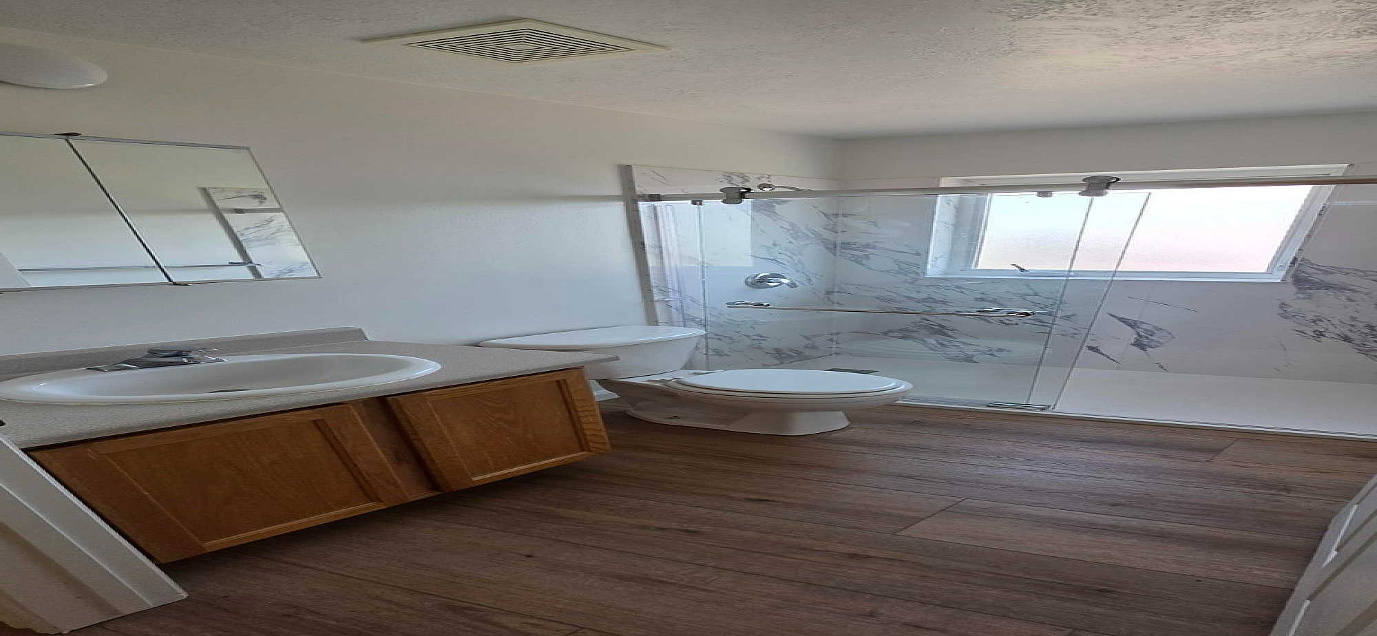 Bright bathroom featuring elegant marble-style tiles, a sleek glass shower door, and warm wood flooring.