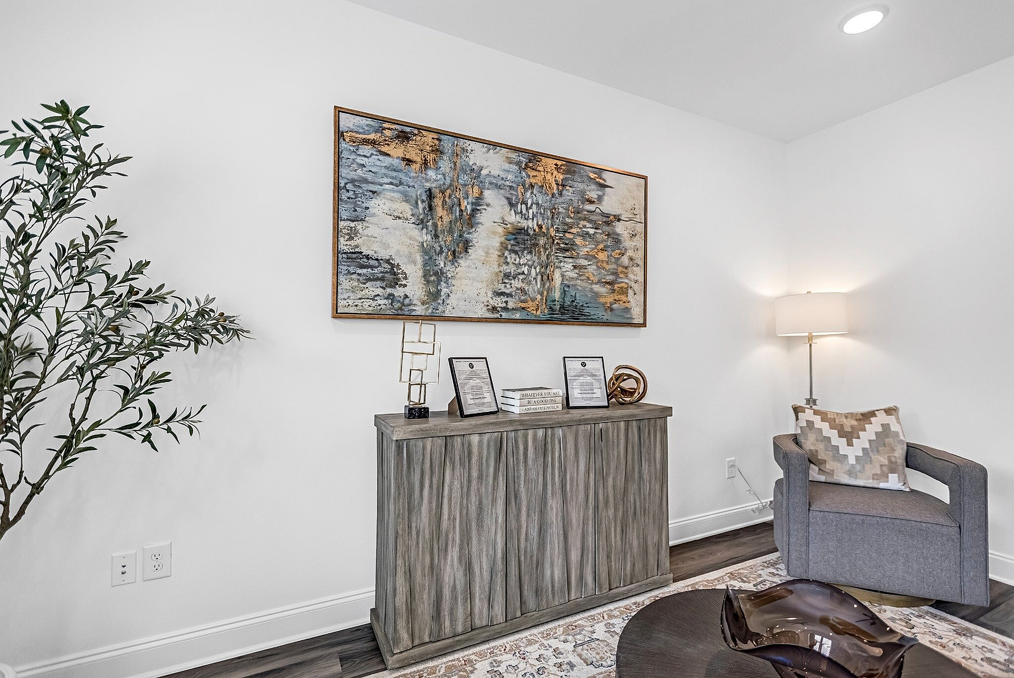 Modern living room corner featuring elegant artwork, a chic gray chair, and a stylish wooden console with decorative items.