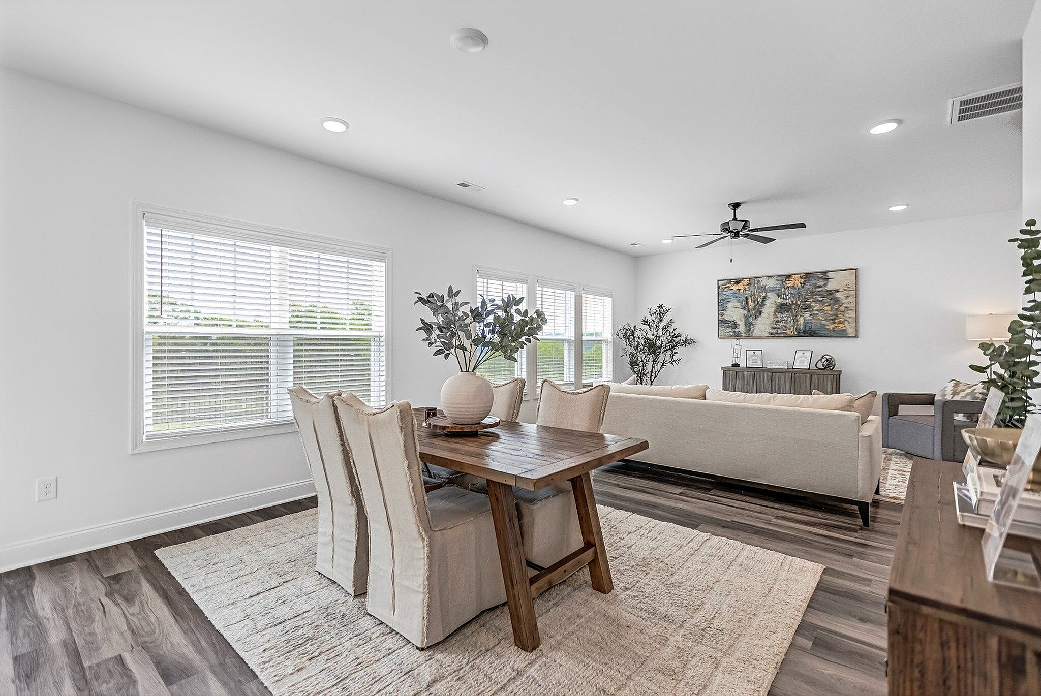 Inviting living and dining area with abundant natural light, featuring elegant furniture, cozy decor, and modern ceiling fan.