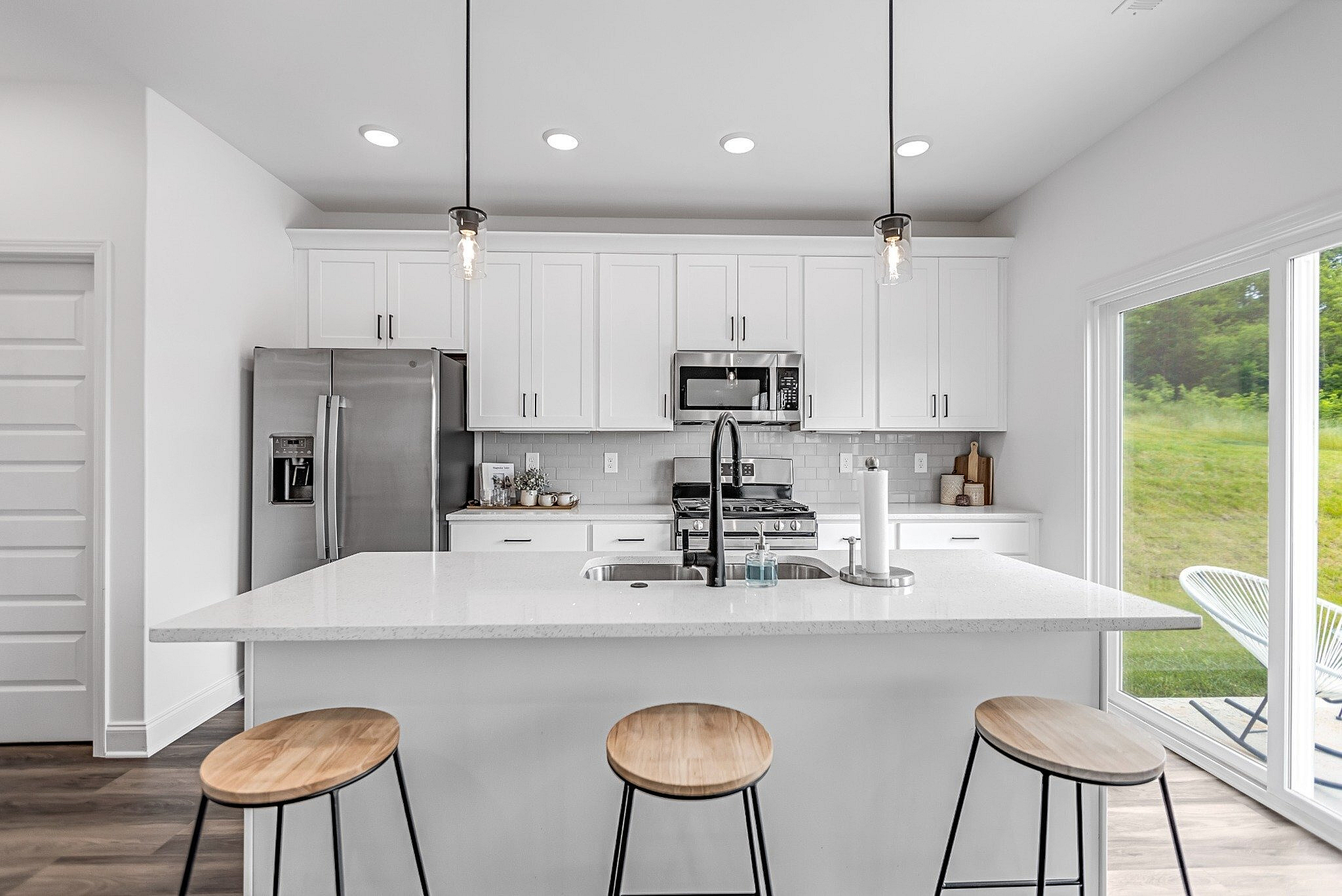 Modern kitchen with sleek white cabinets, stainless steel appliances, and a spacious quartz countertop island with stylish pendant lighting and bar stools.