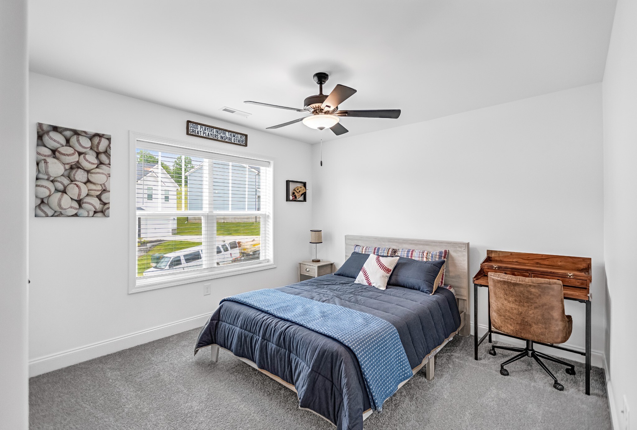 Bright and welcoming bedroom with stylish decor, featuring a comfortable bed, wooden desk, and large window with scenic neighborhood views.