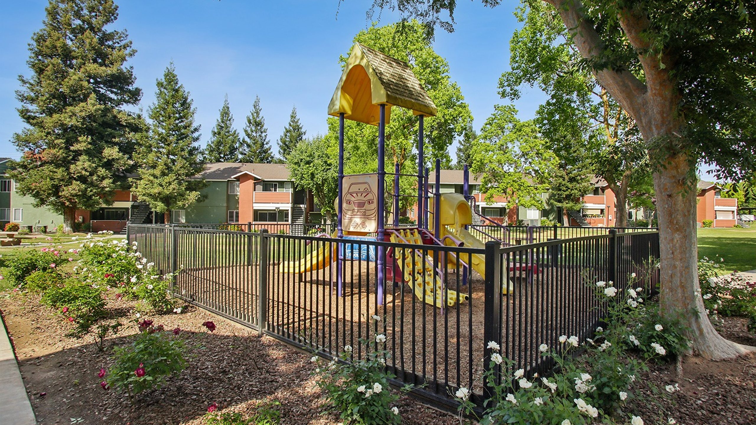 Charming fenced playground surrounded by lush greenery and vibrant rose bushes in a serene residential community.