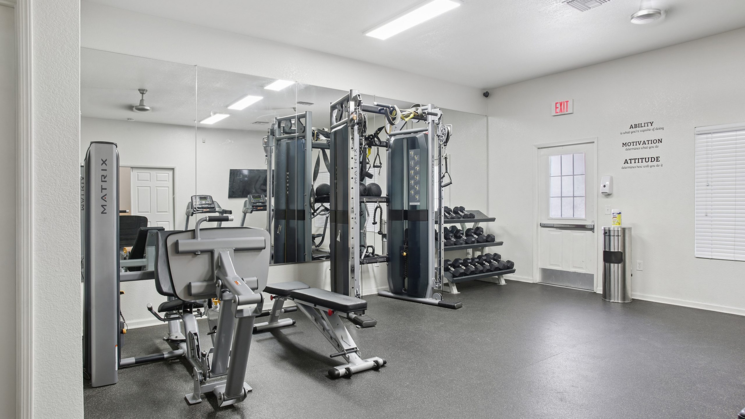Modern apartment gym with state-of-the-art exercise equipment, sleek design, and motivational wall quotes.