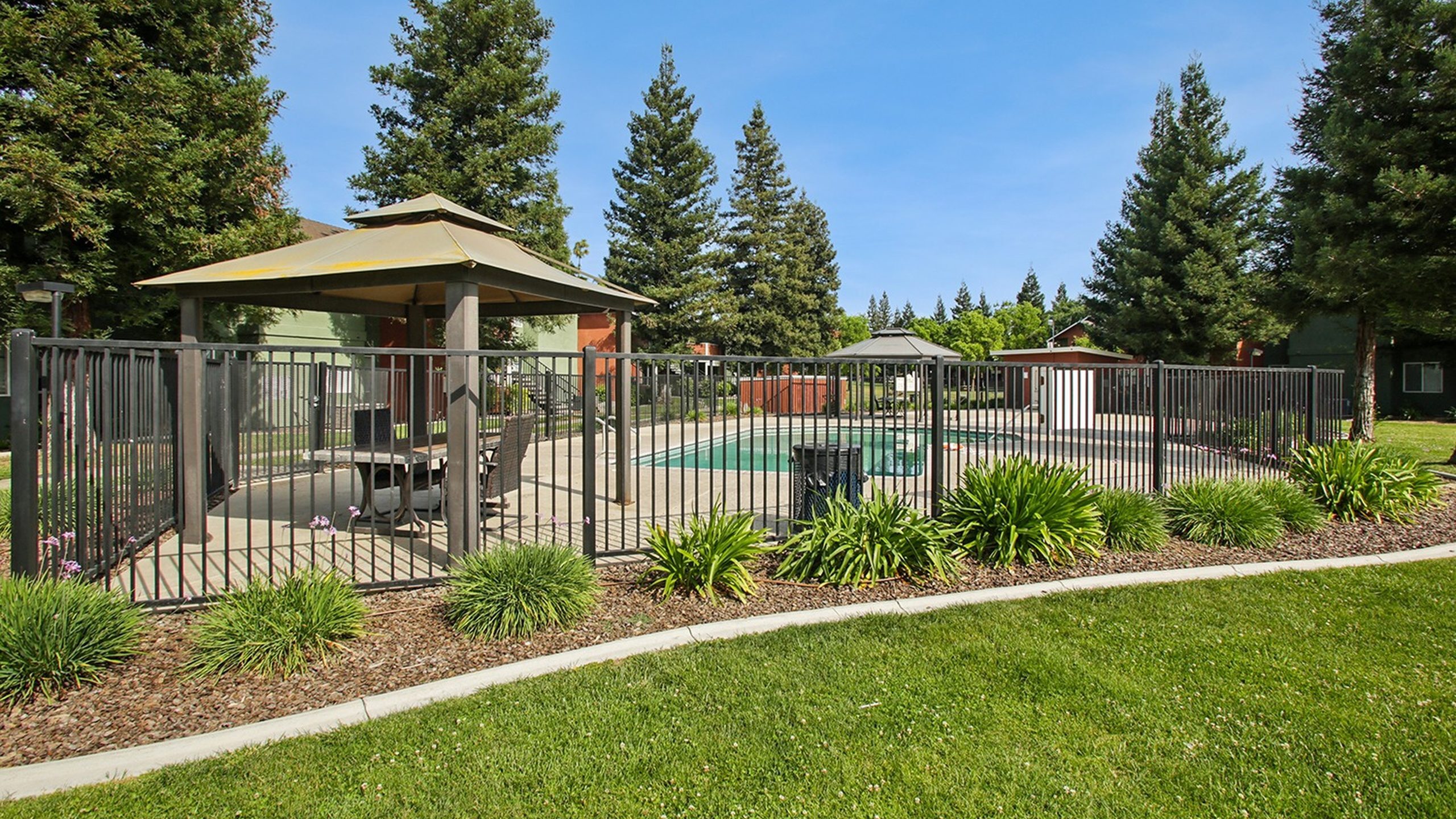 Inviting apartment community outdoor area with a refreshing pool, elegant gazebo, and lush greenery, perfect for relaxation and enjoyment.