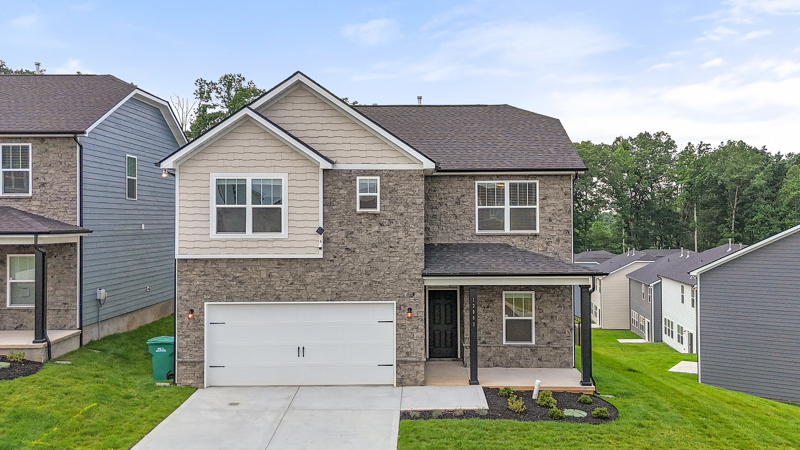 Charming two-story home with a modern design, featuring a welcoming porch, double garage, and surrounded by lush greenery in a serene neighborhood.