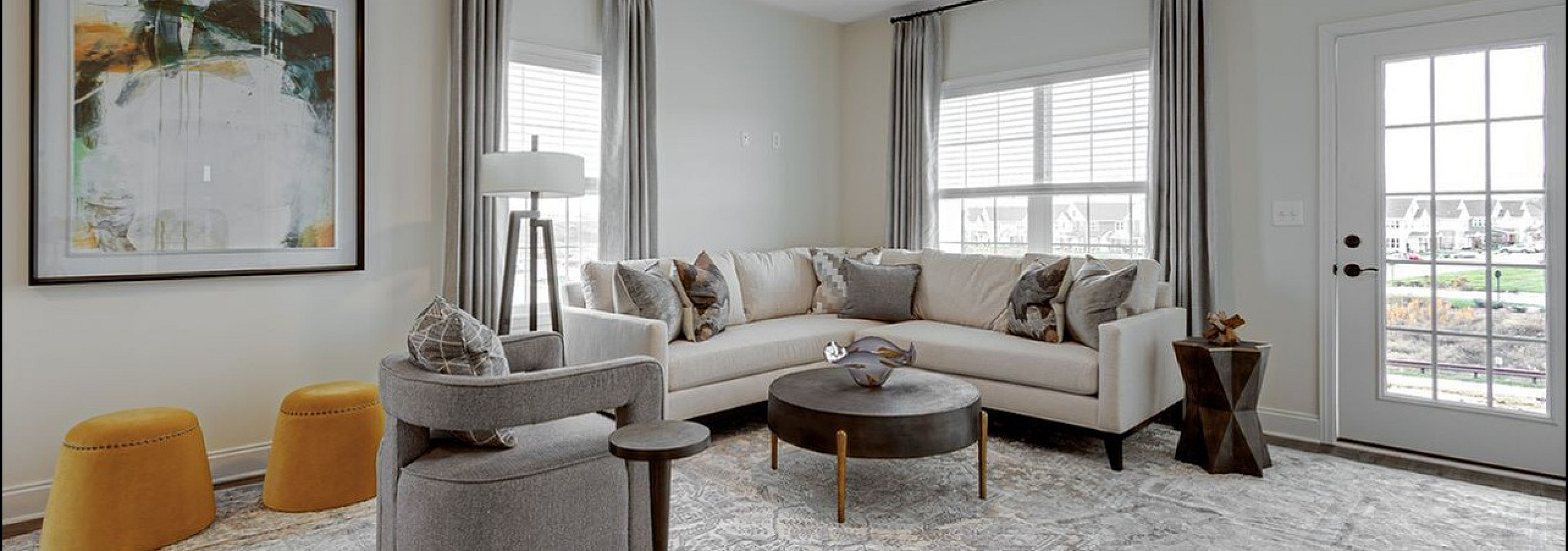 Chic living room with modern decor, featuring a cozy beige sectional, stylish round coffee table, and large art piece, bathed in natural light from elegant French doors.