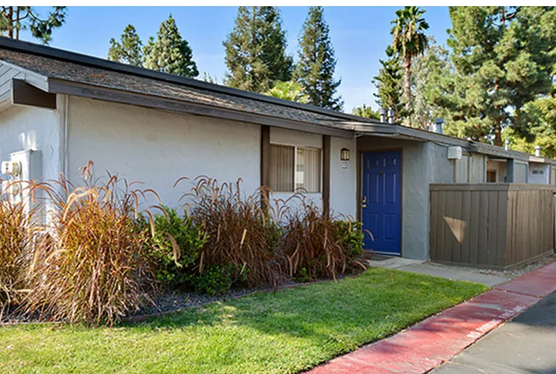 Charming suburban apartment exterior with vibrant greenery, blue front door, and a welcoming pathway.