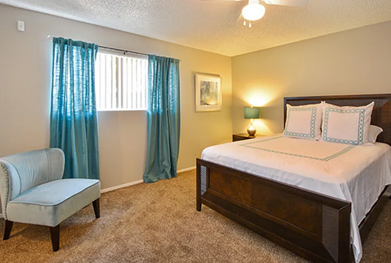 Inviting bedroom with a cozy ambiance, featuring a plush bed, elegant blue chair, and soft lighting.