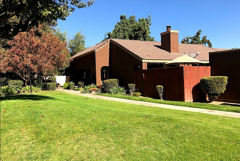 Charming suburban residence with elegant brown brickwork, lush green lawn, and a cozy patio area, perfect for peaceful living.