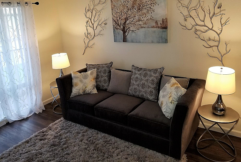 Cozy living room with elegant decor featuring a plush dark sofa, stylish lamps, and tree-themed wall art, perfect for relaxation.