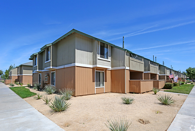 Charming apartment complex with modern two-story buildings, featuring well-maintained landscaping and a clear blue sky.