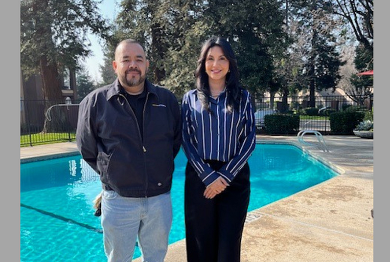 Friendly duo smiling by a sparkling outdoor pool, surrounded by lush greenery and serene ambiance.