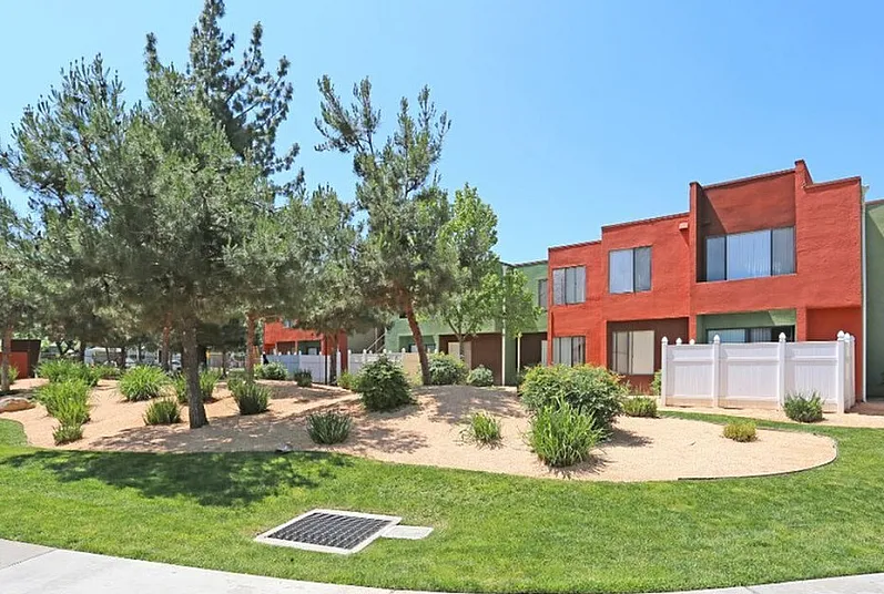 Charming apartment complex with vibrant red and green exterior, surrounded by lush landscaping and mature trees, perfect for a serene living environment.